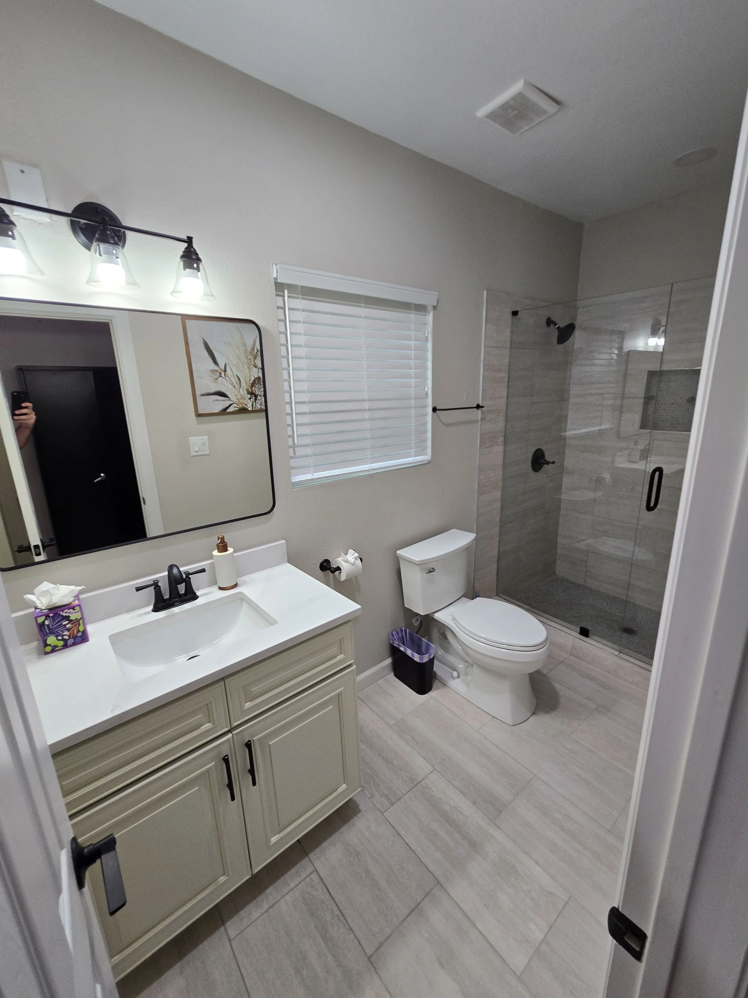 A clean bathroom with a vanity and sink, mirror, toilet, window, and walk-in shower with glass doors.