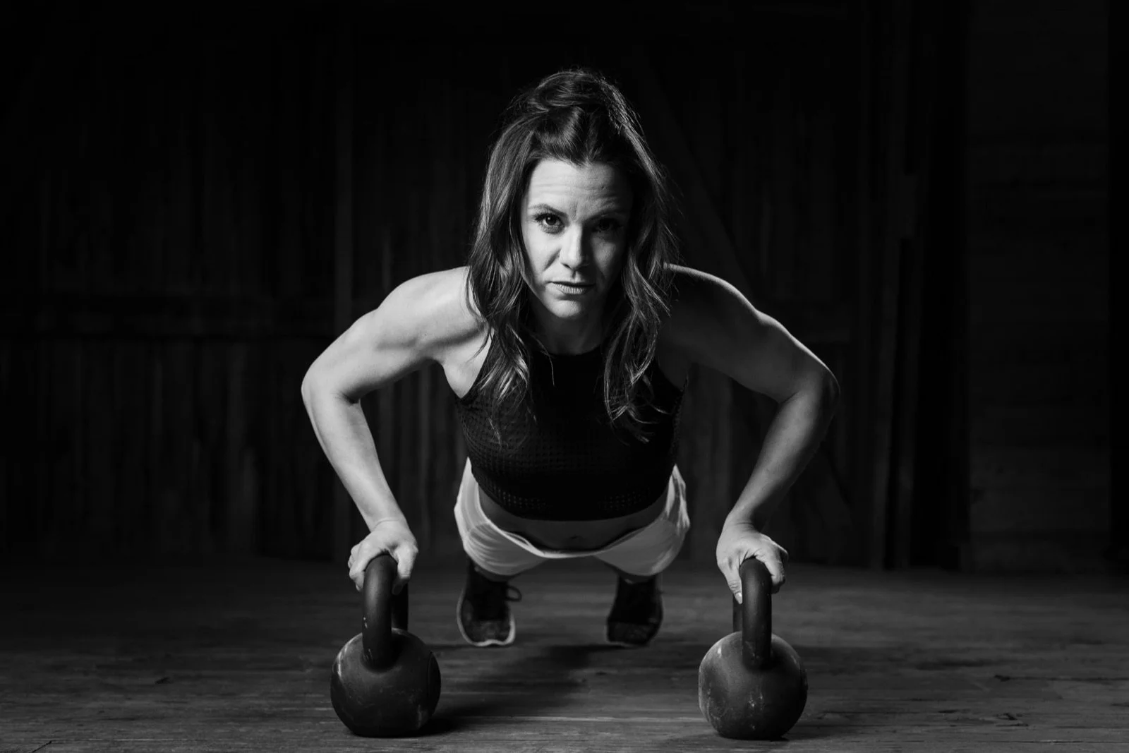 Black and white photo of a woman doing a push-up on kettlebells.