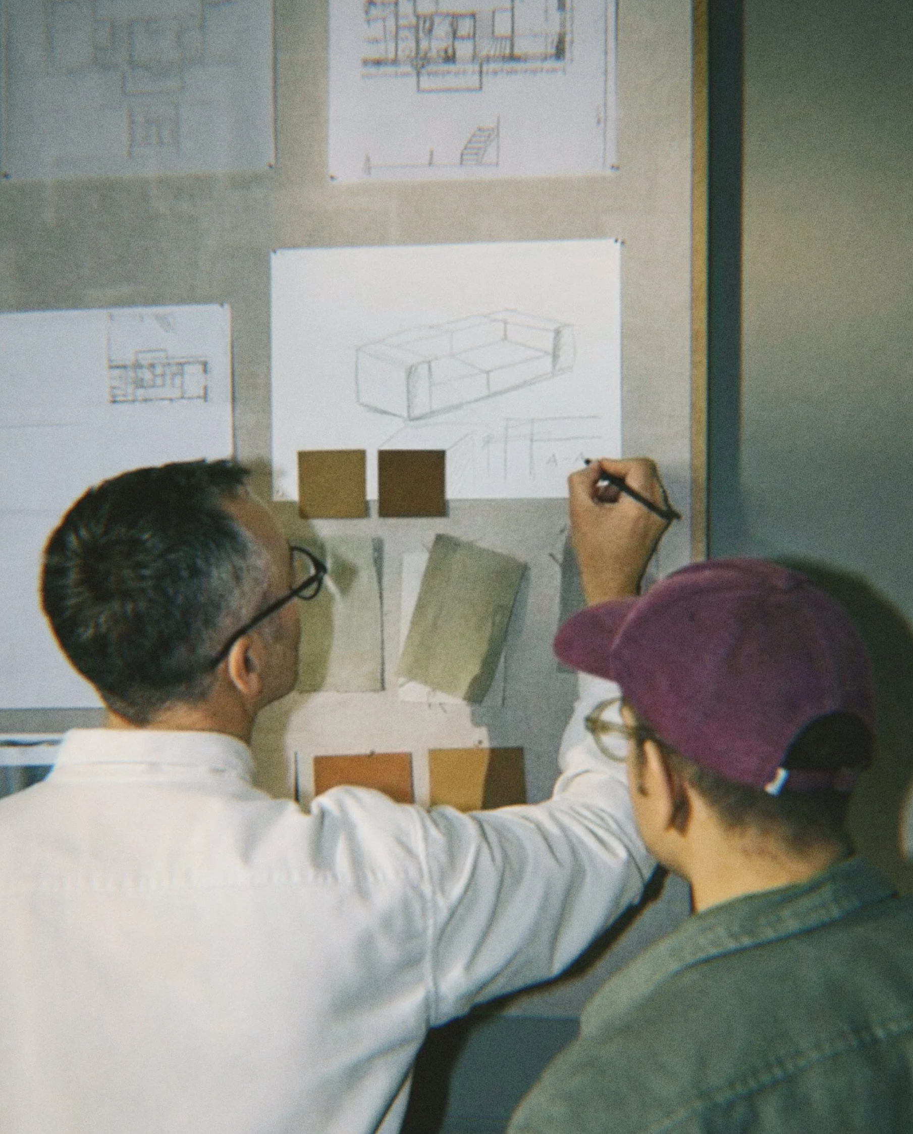 Dois homens observando um painel com desenhos de projetos de interiores e amostras de cores e materiais