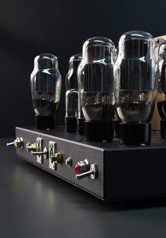 Nahaufnahme eines Röhrenverstärkers mit sichtbaren Elektronenröhren auf einer schwarzen Oberfläche vor dunklem Hintergrund.