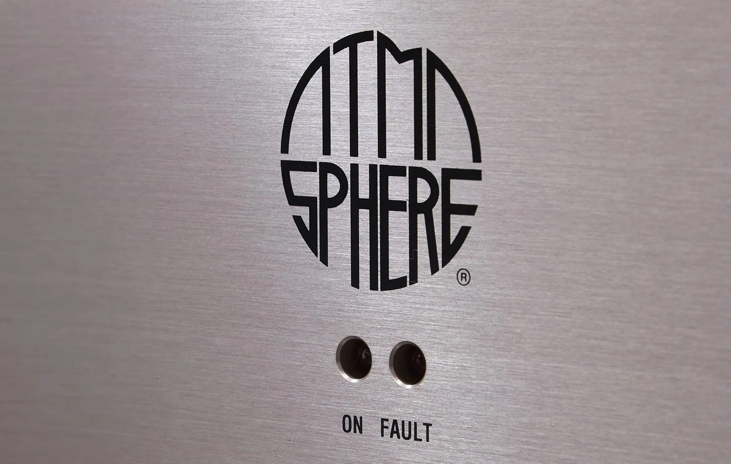 Das Bild zeigt eine Metallfläche mit einem Logo, das den Schriftzug 'ATMOSPHERE' in einer ovalen Form enthält. Darunter befinden sich zwei kleine Löcher mit den Beschriftungen 'ON' und 'FAULT' darunter.
