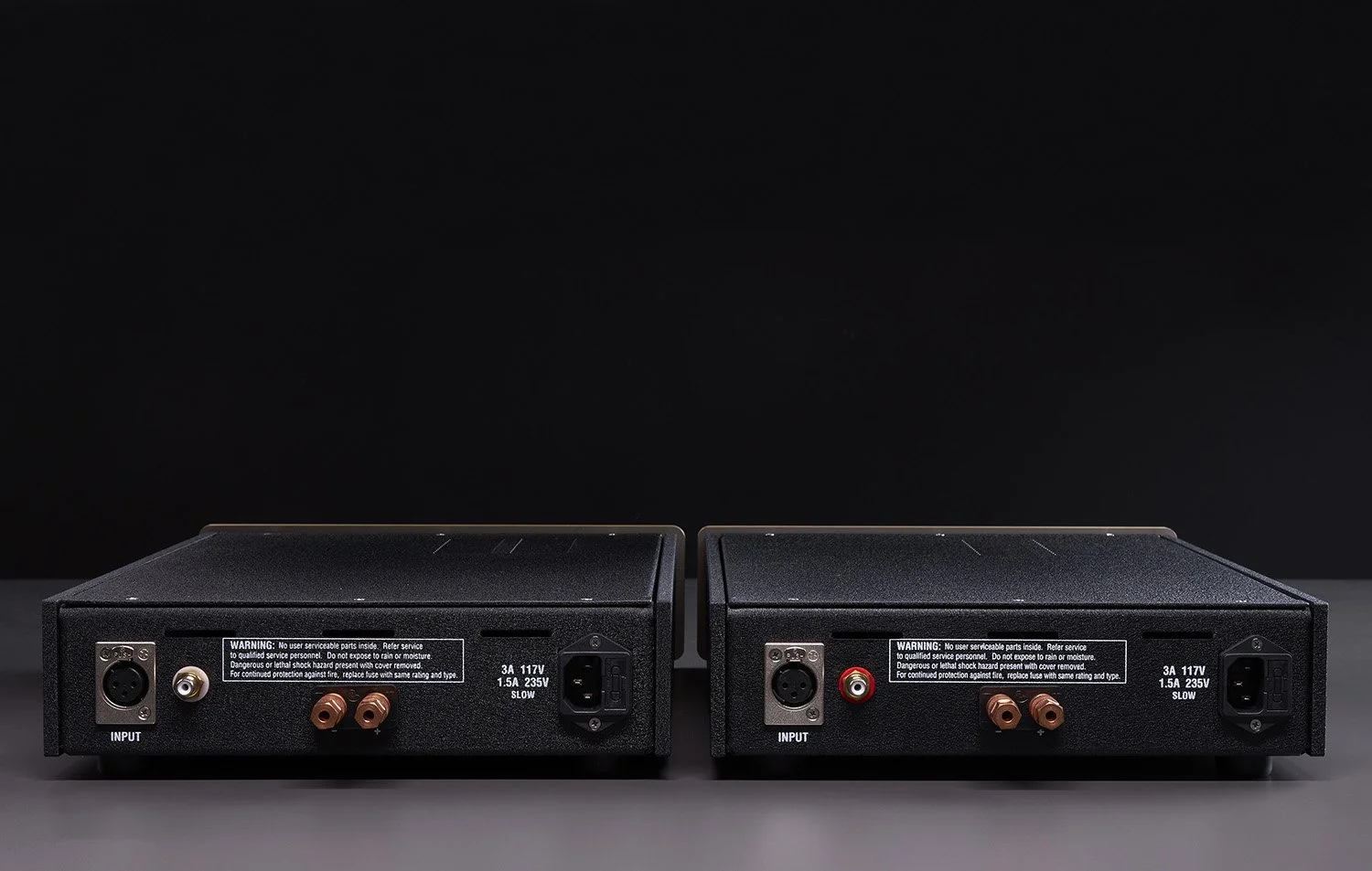 Zwei schwarze Audioverstärker mit verschiedenen Anschlussbuchsen auf einer schwarzen Oberfläche, vor einem schwarzen Hintergrund.