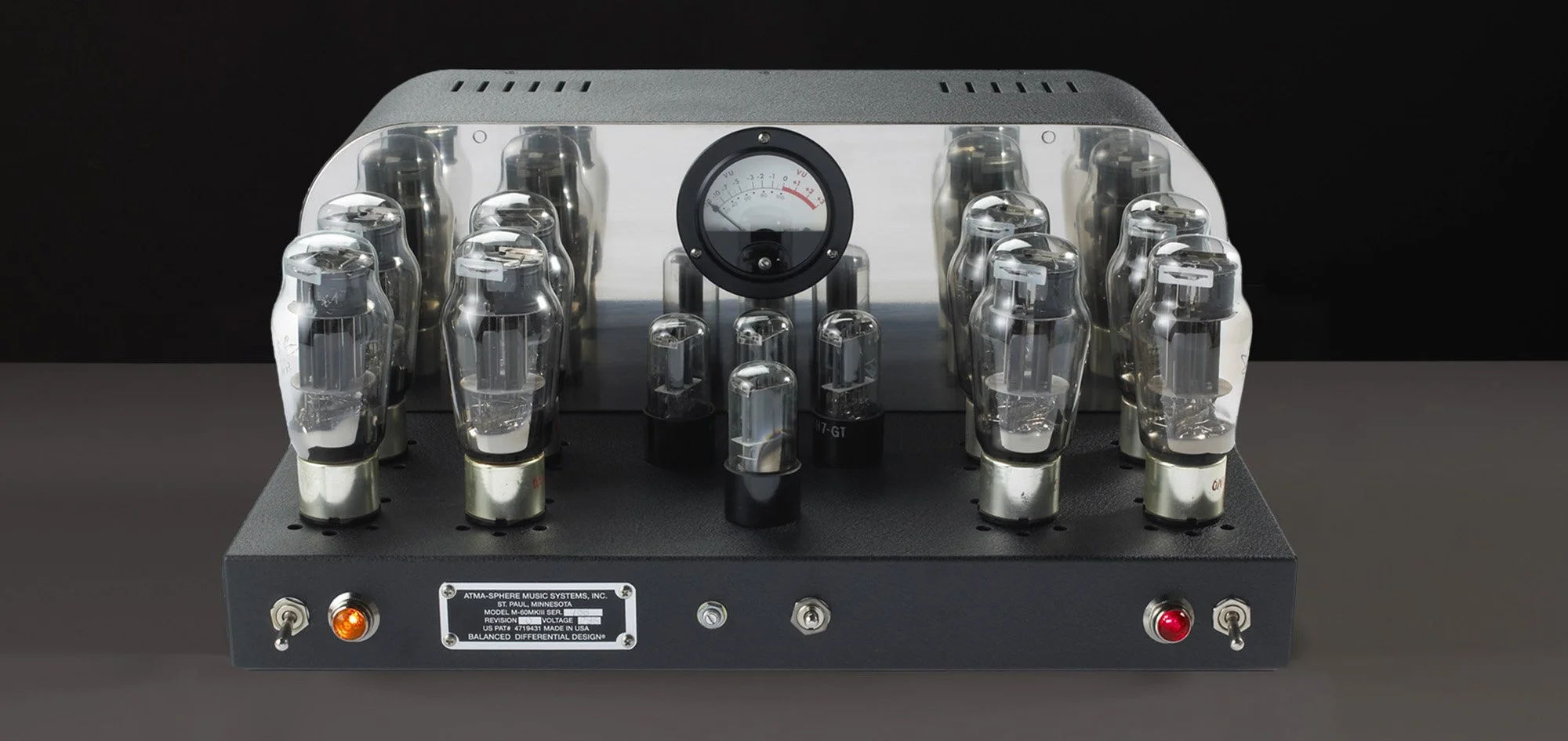 Ein vintage Röhrenverstärker mit mehreren Vakuumröhren, ein Umdrehungmesser und Kontrollleuchten, auf einem Tisch gegen einen schwarzen Hintergrund.
