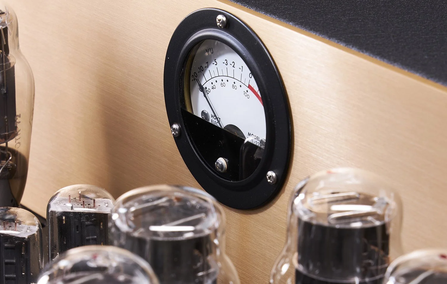 Ein VU-Meter zeigt eine fast maximale Lautstärke an, eingebaut in eine Holzwand, umgeben von Vakuumröhren.