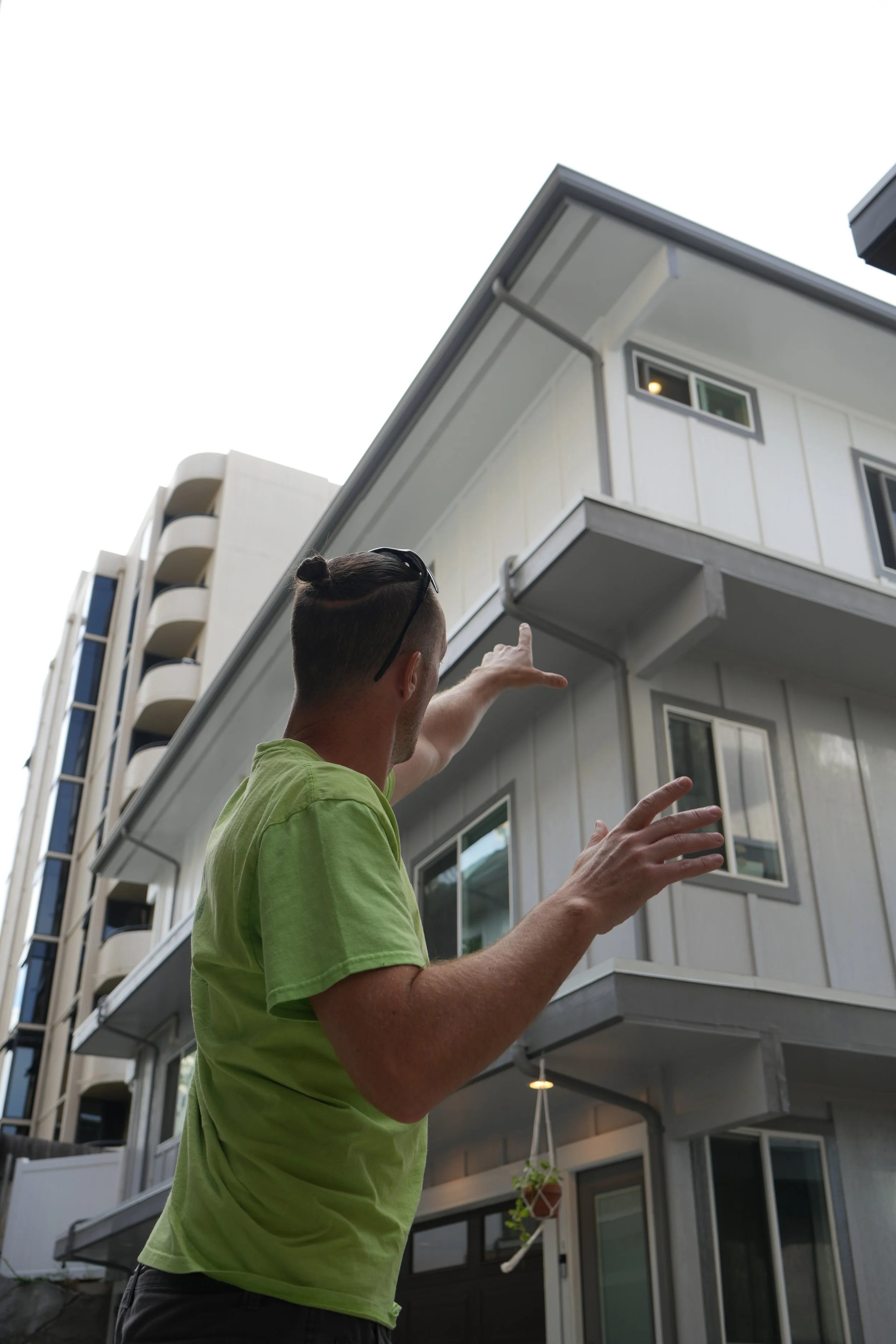 A person pointing at a modern, multi-story residential building with white exterior walls and multiple windows.