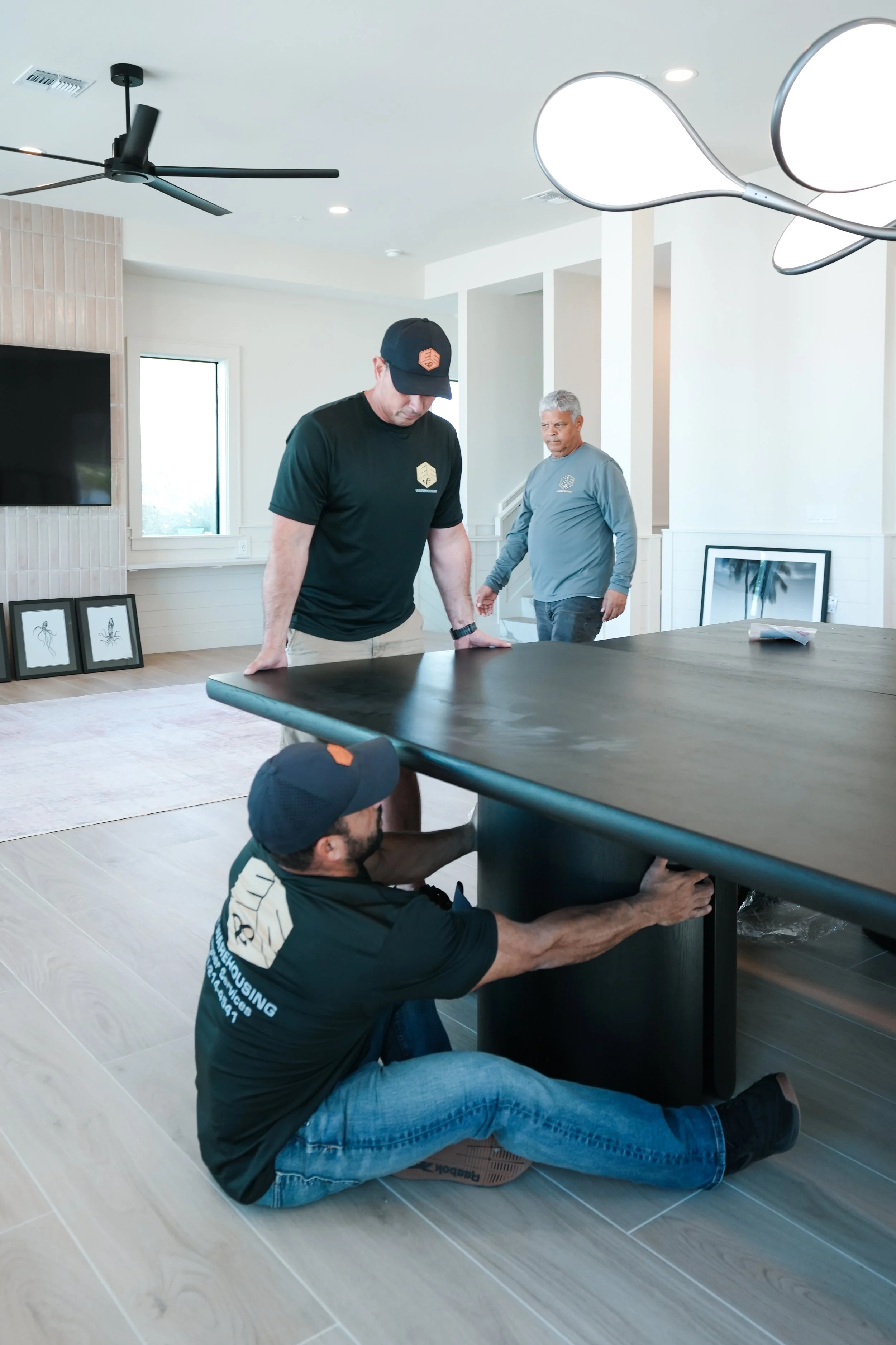 Three men assembling a large dark wooden table in a bright living room with modern decor.