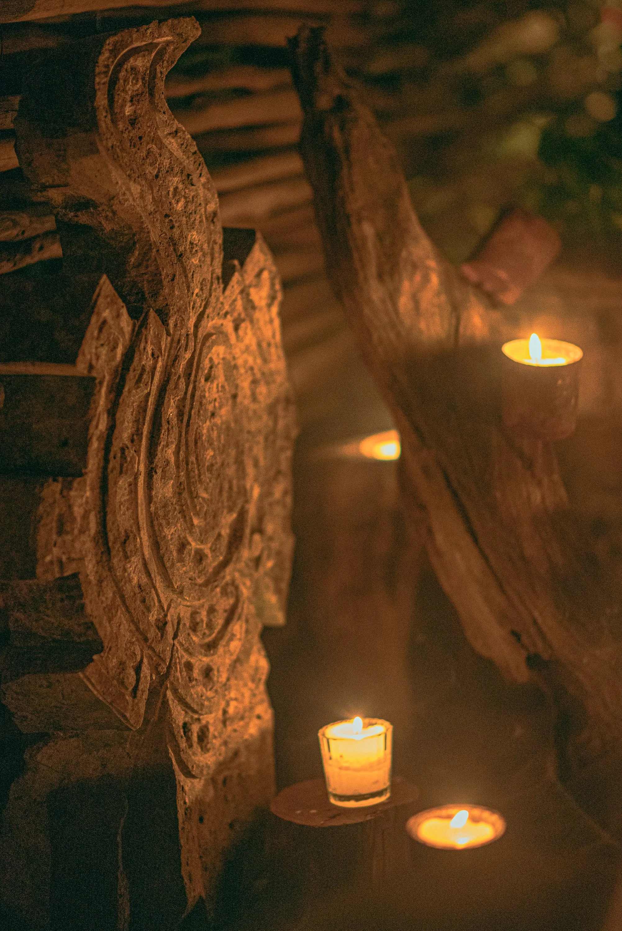 Close-up of several lit candles on wooden surfaces with a rustic, logs and textured bark background, creating a warm and cozy ambiance.