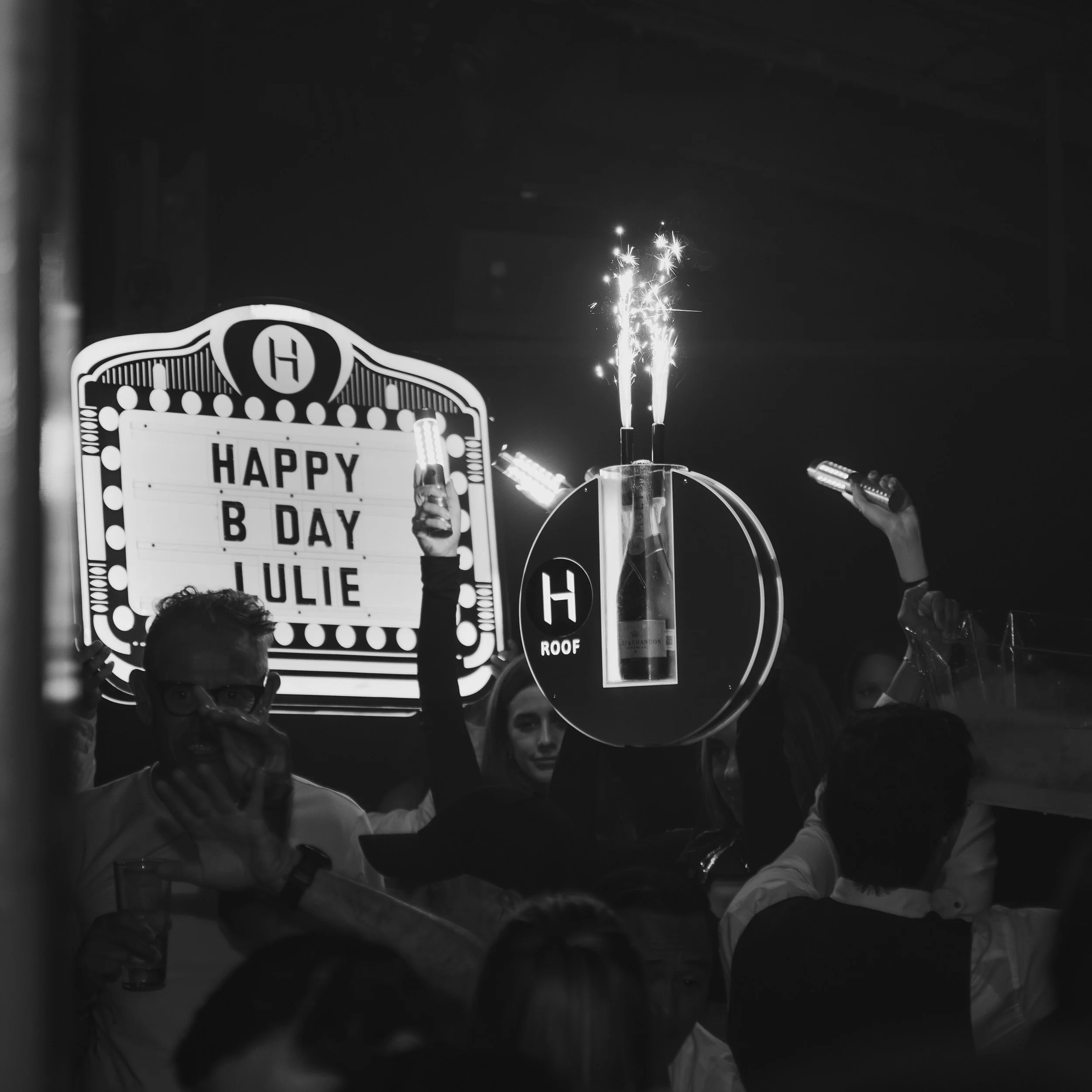 Celebration with sparklers and a sign that reads 'HAPPY B DAY LULIE' at a lively party.