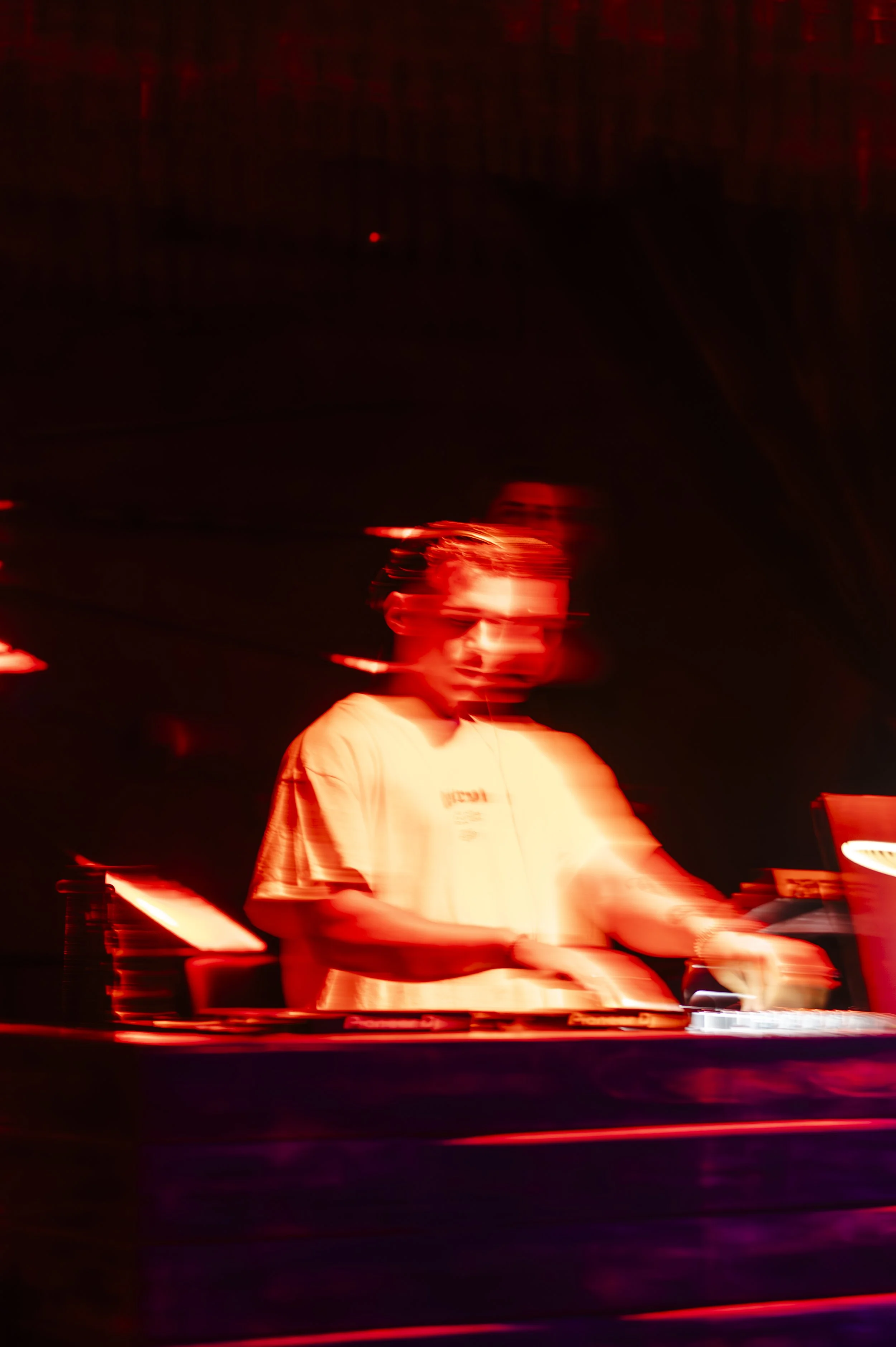 A person DJing at a music event with red lighting and motion blur.