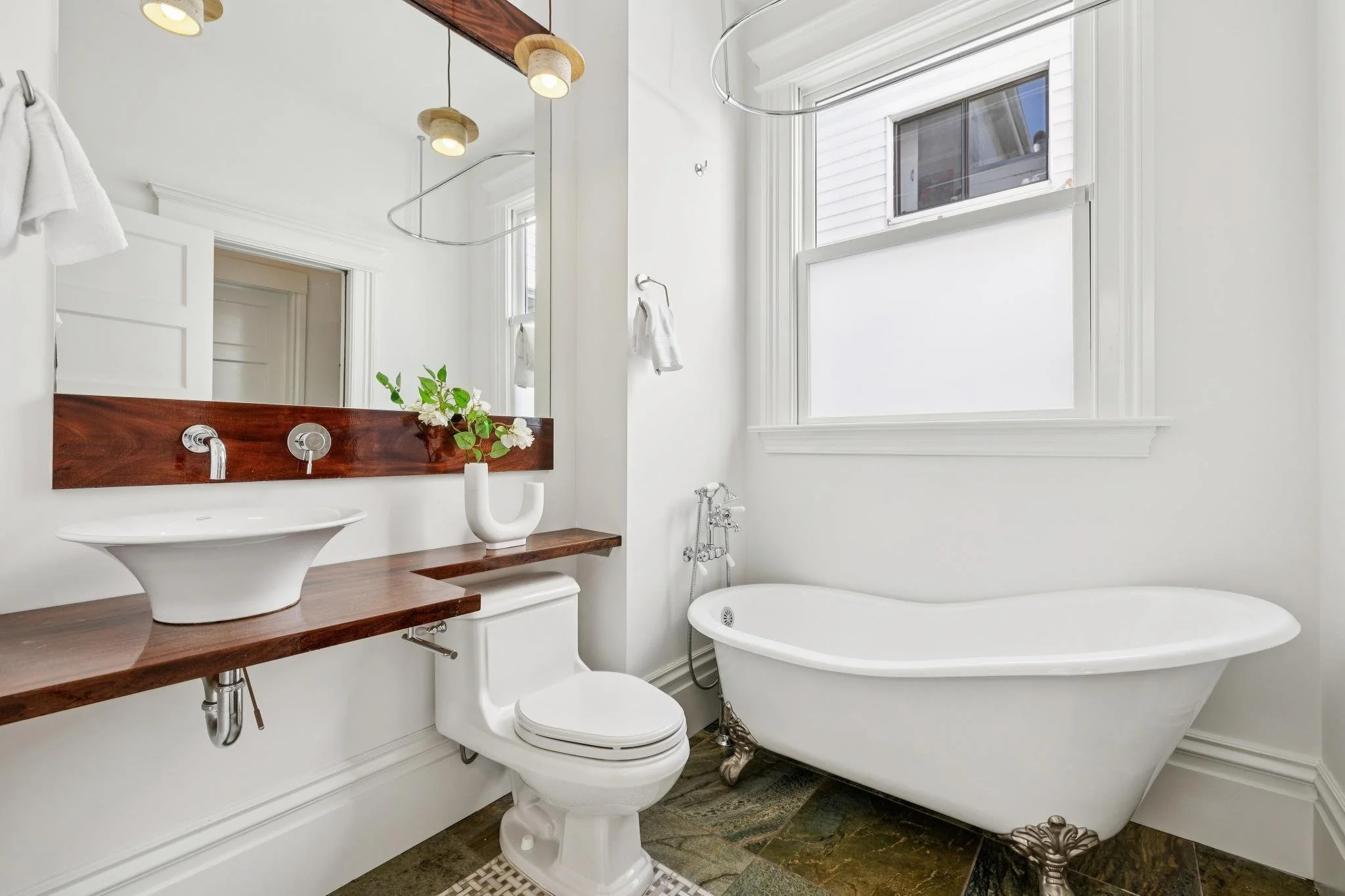 Bathroom featuring a clawfoot bathtub, a toilet, a wooden countertop with a vessel sink, a large mirror, and a window with frosted glass.