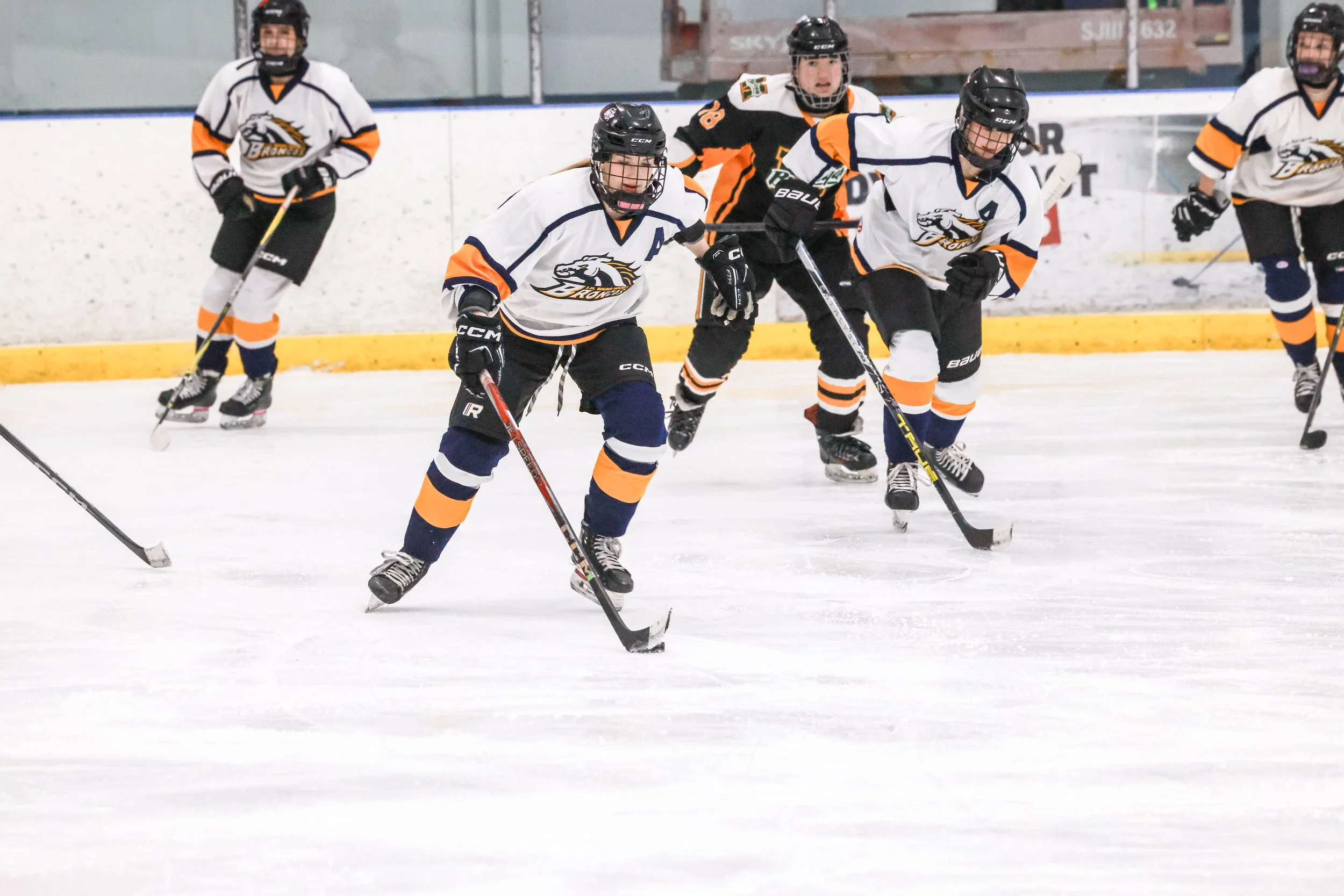 Hockey players in white and black jerseys on ice rink, engaged in a game.