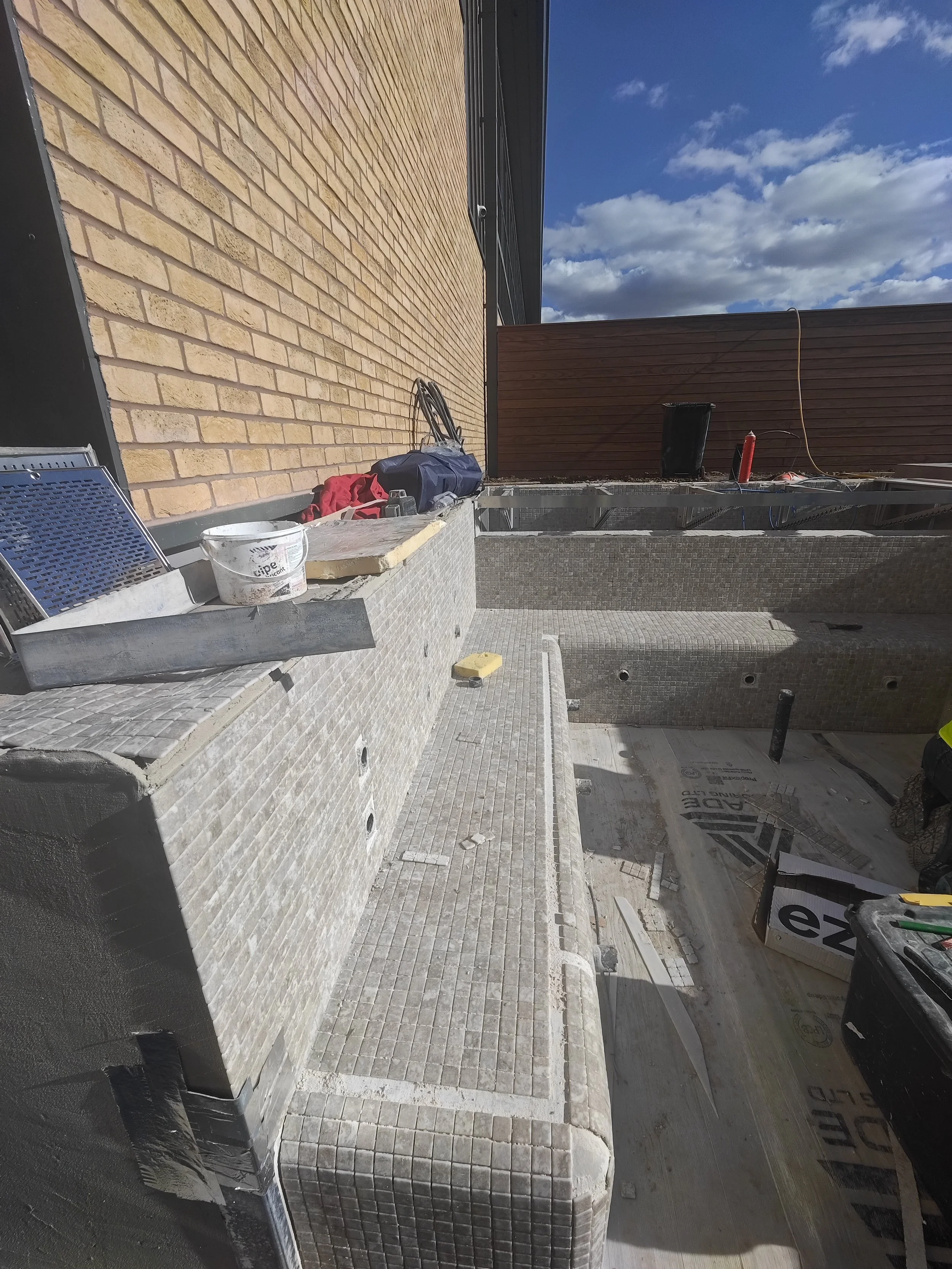Construction site with tiled steps, brick wall, tools, and construction materials visible.