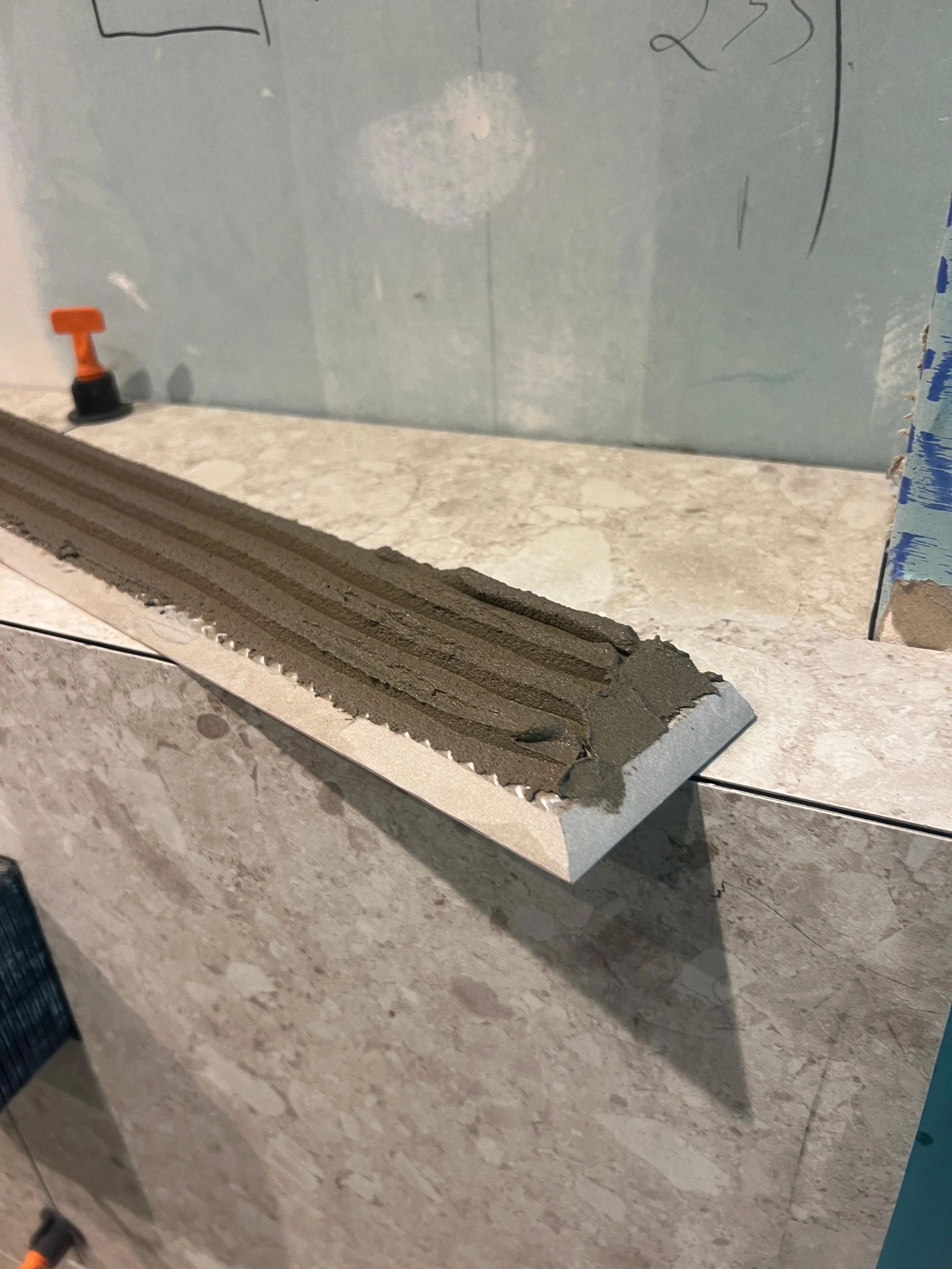 A bathroom countertop with a square tile and a section of wet cement or mortar on it, with construction tools and materials visible.