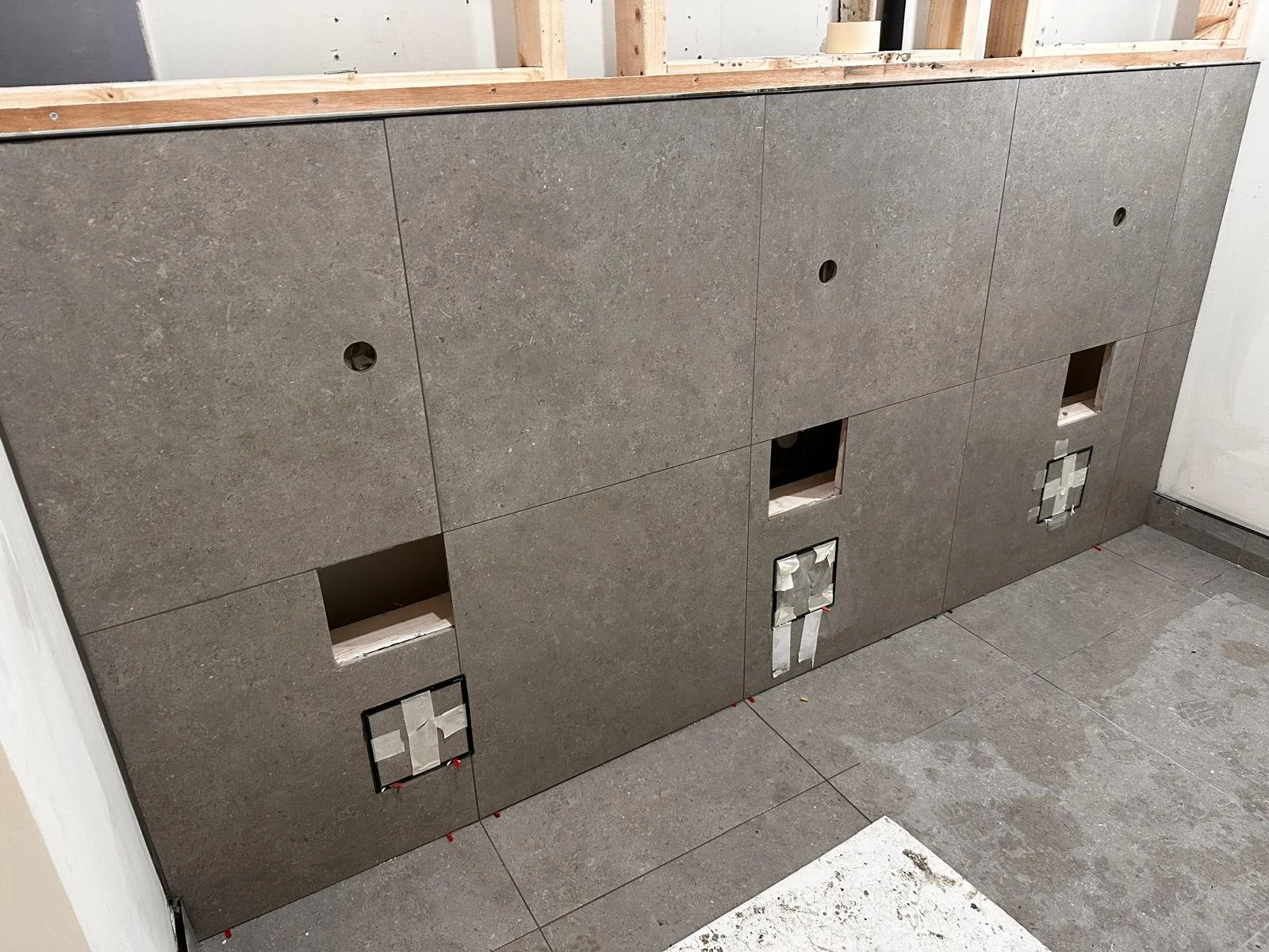 Kitchen or bathroom cabinetry with unfinished gray stone-like panels, with cutouts for handles and appliances, under construction or renovation.