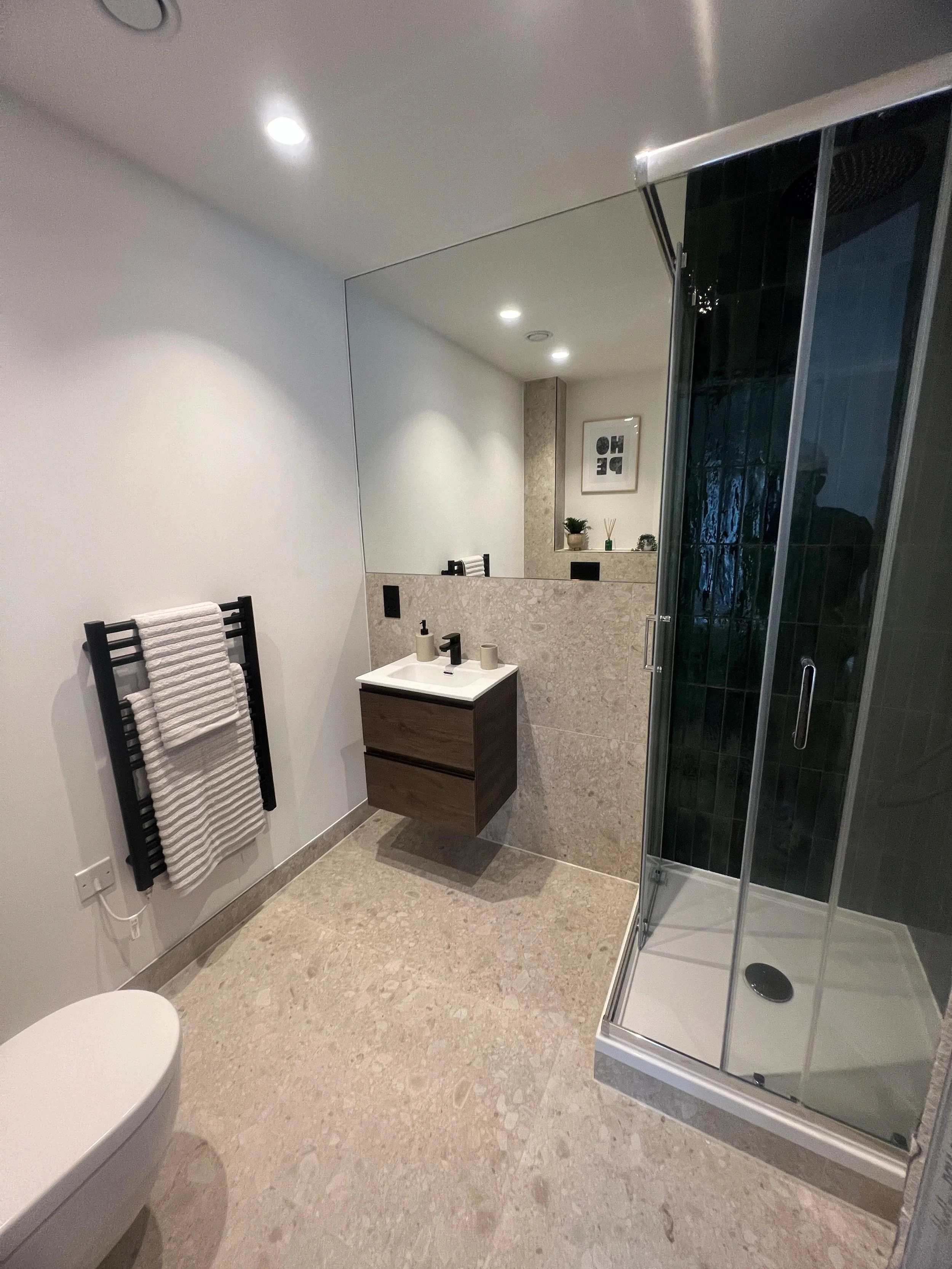Modern bathroom with a shower, small sink, towel rack with towels, framed decorative art, and a mirror.