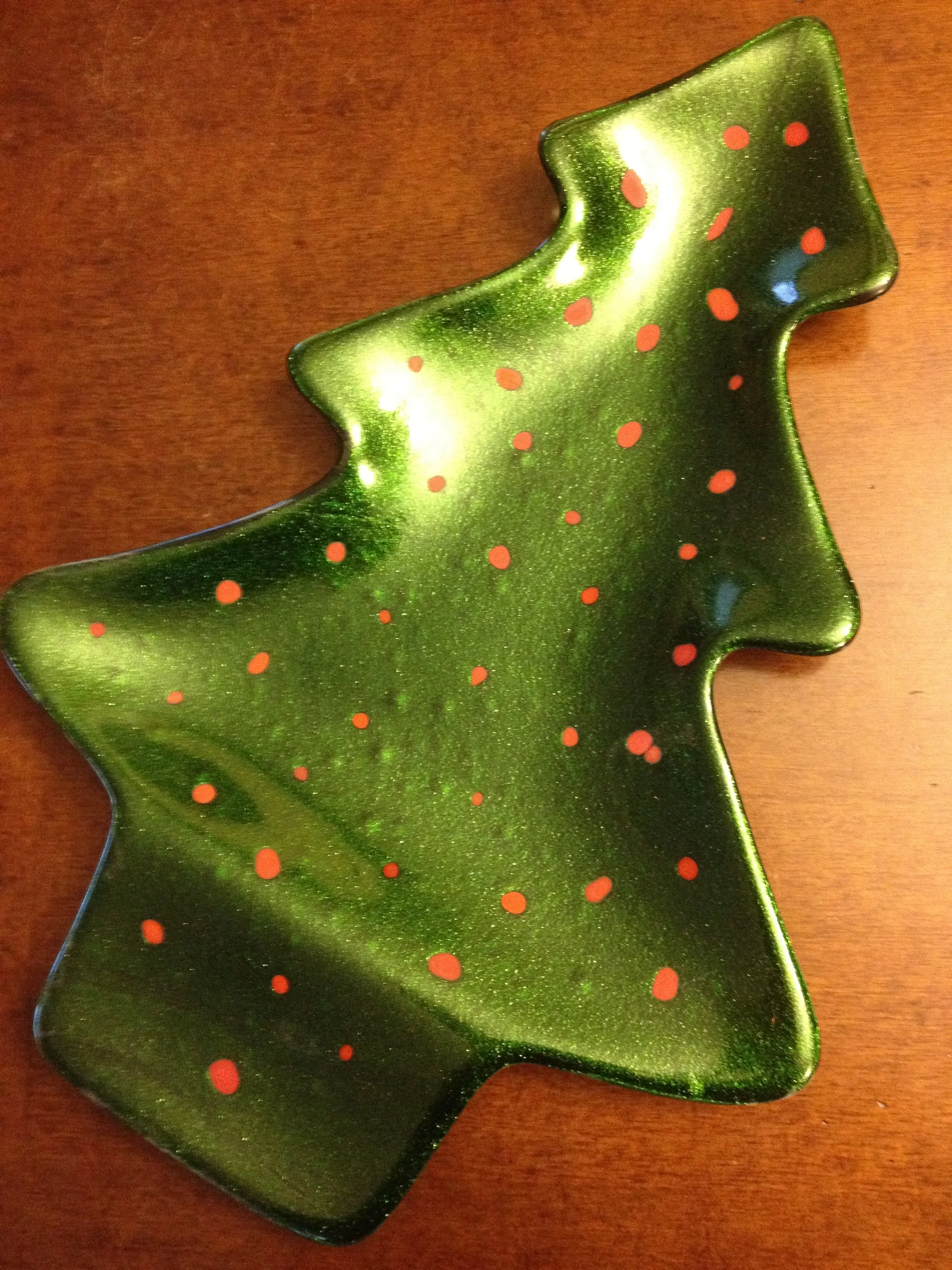 Green glass dish shaped like a Christmas tree with orange dots, placed on a wooden surface.