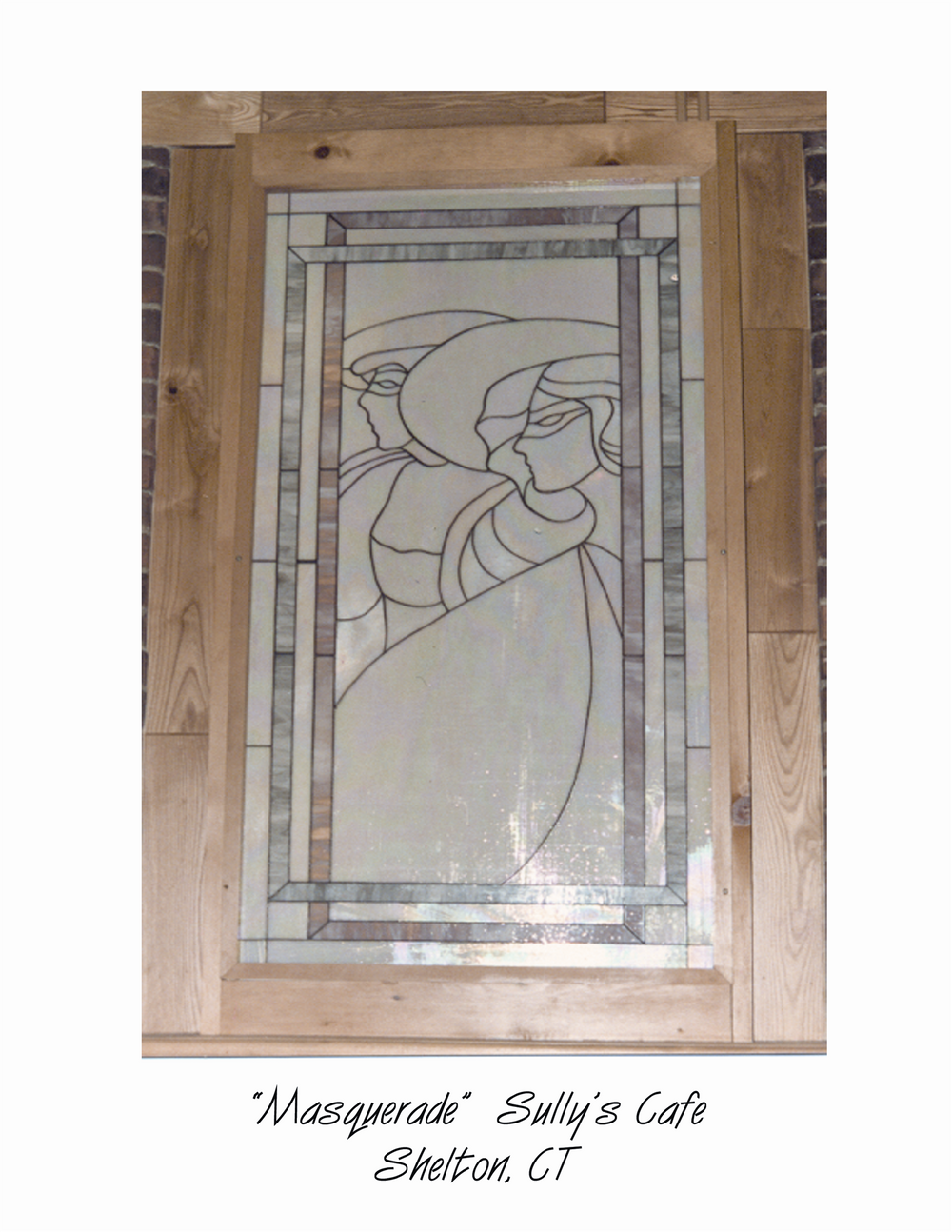 A stained glass artwork titled 'Masquerade' depicting two faces in profile leaning towards each other, framed by a wooden border, located in Sully's Cafe, Shelton, CT.