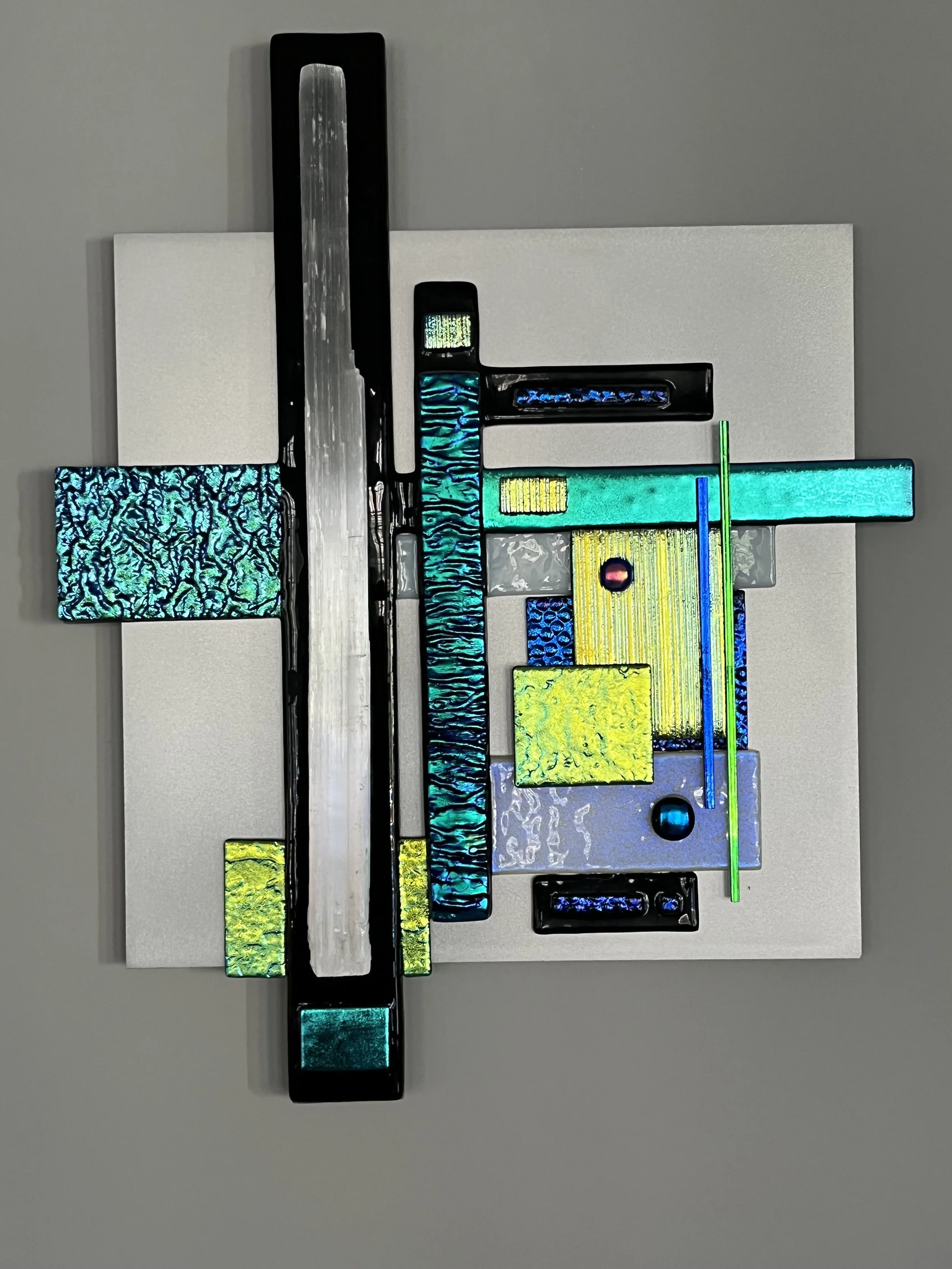 Colorful abstract glass artwork with various rectangular and linear shapes mounted on a white background.