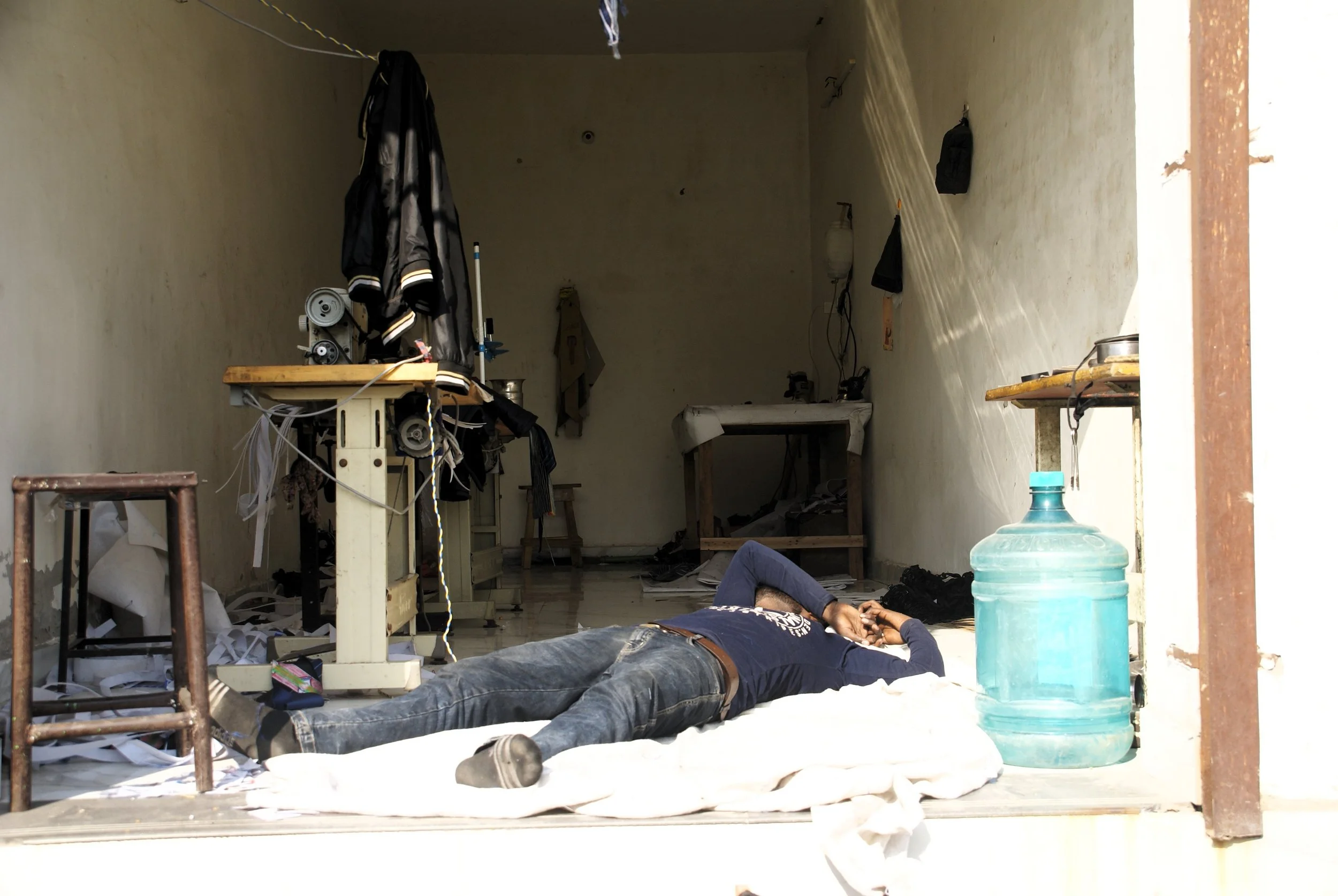 A young garment worker rests on the floor of his workshop in a rural village, taking a short break from work in the afternoon heat.