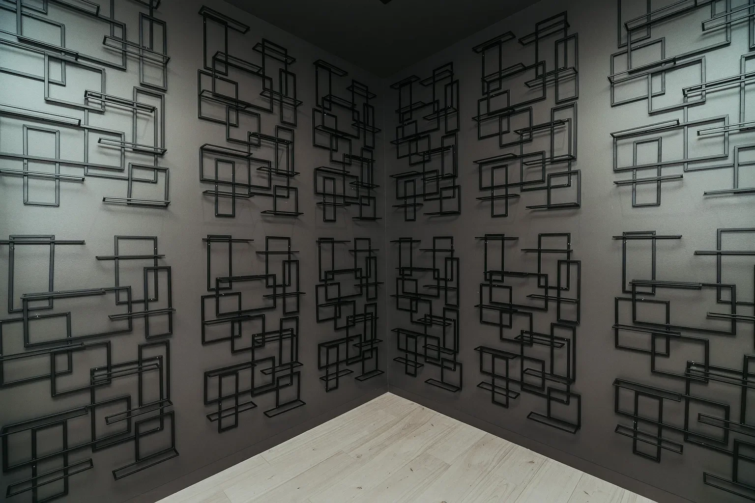 Corner of a room with walls decorated with multiple black metal geometric square and rectangular frames, arranged in an abstract pattern.