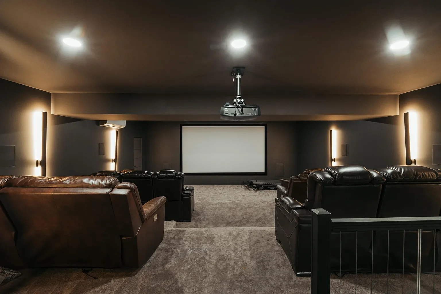 Home theater room with a large projector screen, ceiling-mounted projector, and comfortable leather recliner seating.