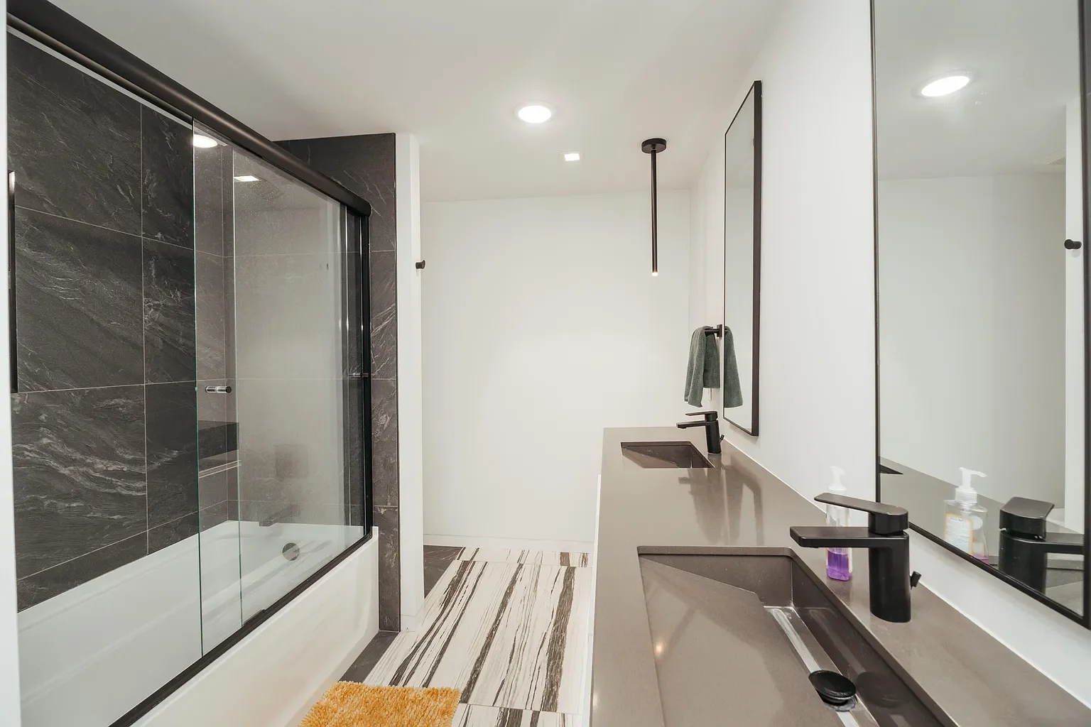 Modern bathroom with a glass-enclosed shower, a double sink vanity with black fixtures, and a large mirror. The bathroom has white walls, marble-patterned floor, and black accents.
