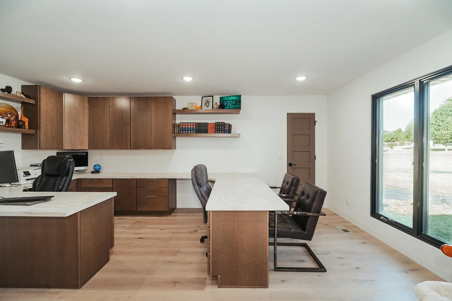Modern conference room with wooden furniture, black chairs, and large window showing outdoor scenery.