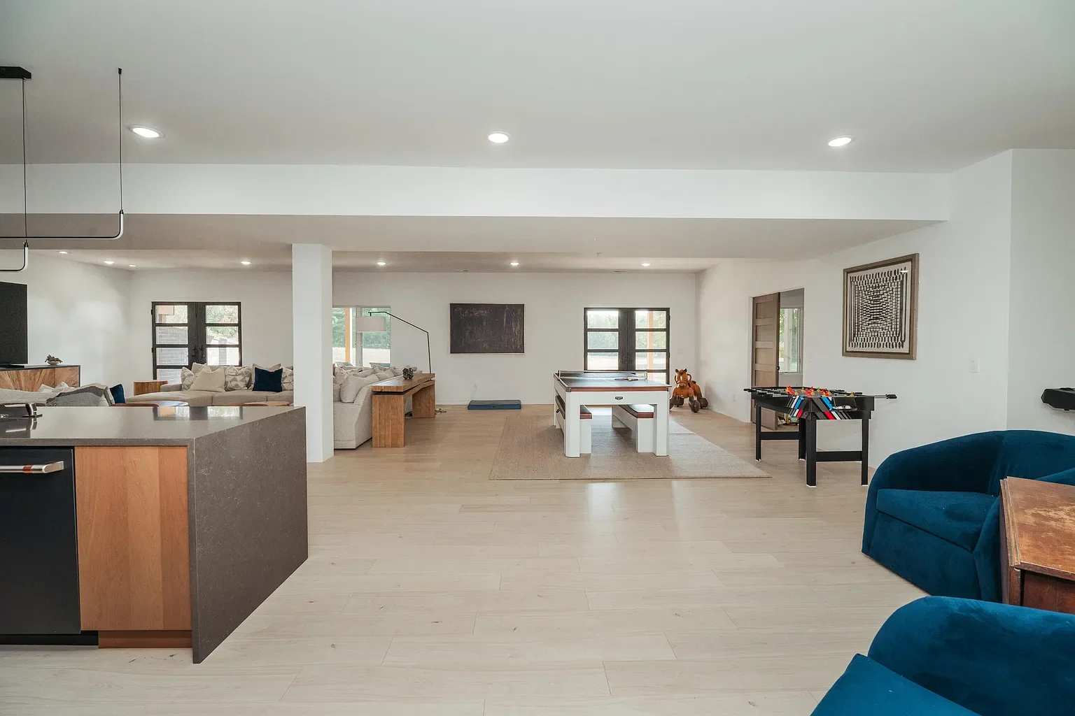 Spacious open-concept living area with a kitchen, sofas, a foosball table, and windows letting in natural light.