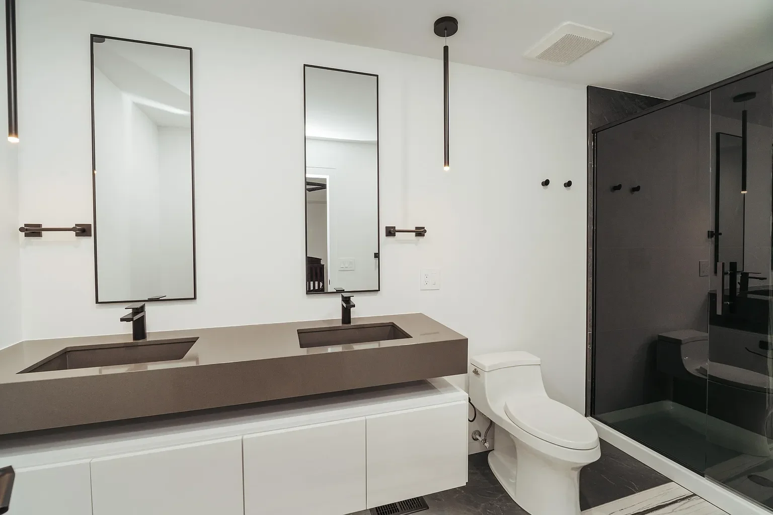 Modern bathroom with double vanity, two mirrors, black fixtures, toilet, and a glass-enclosed shower with black accents.