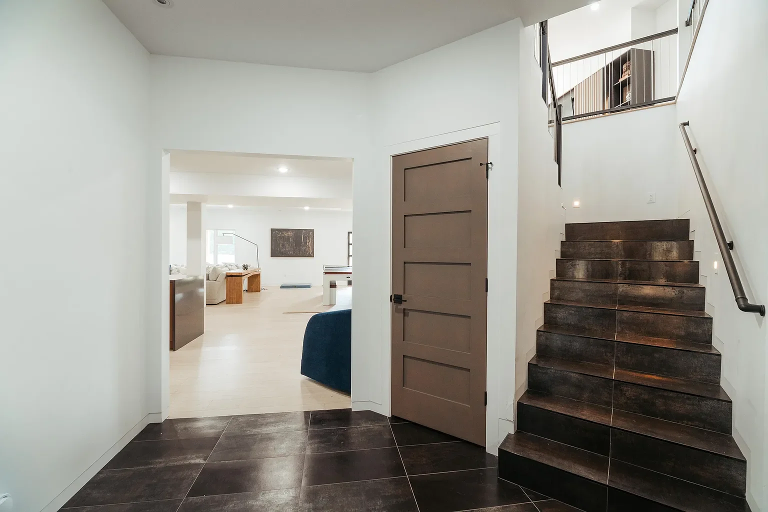 Interior of a modern home with a staircase, a doorway, and living rooms visible in the background