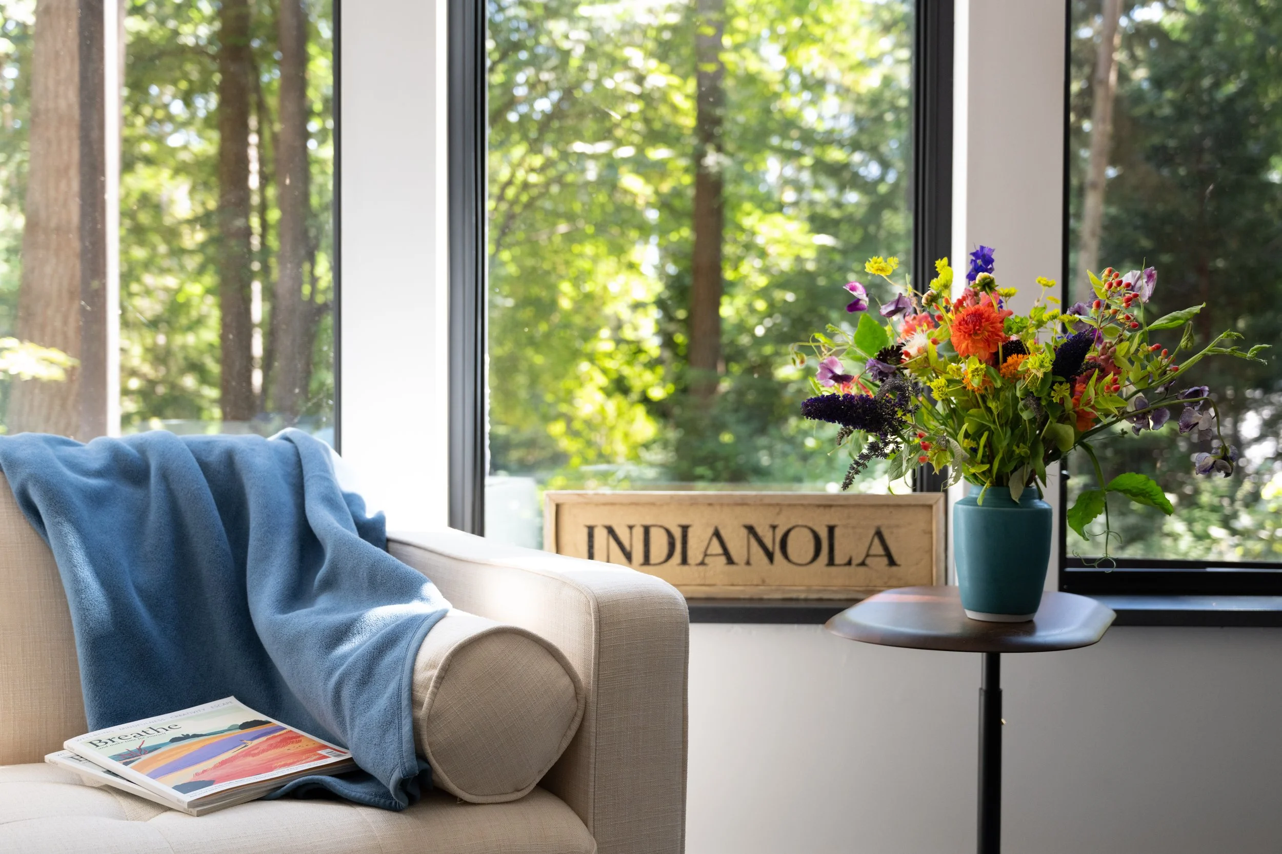 Cozy reading chair next to a bouquet of colorful flowers, with a view of the forest