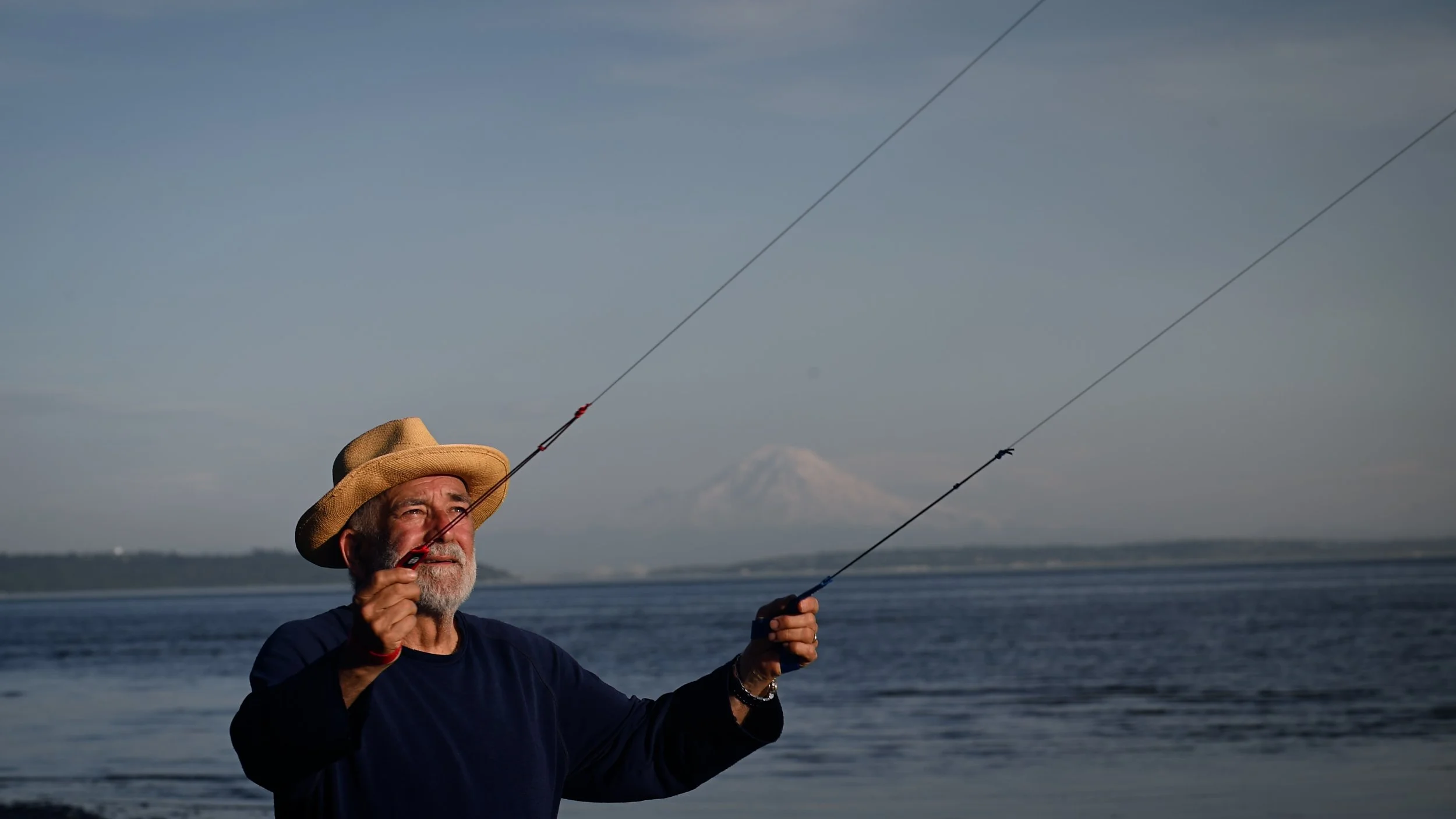 Man flying a kite at the ocean, with mountain view