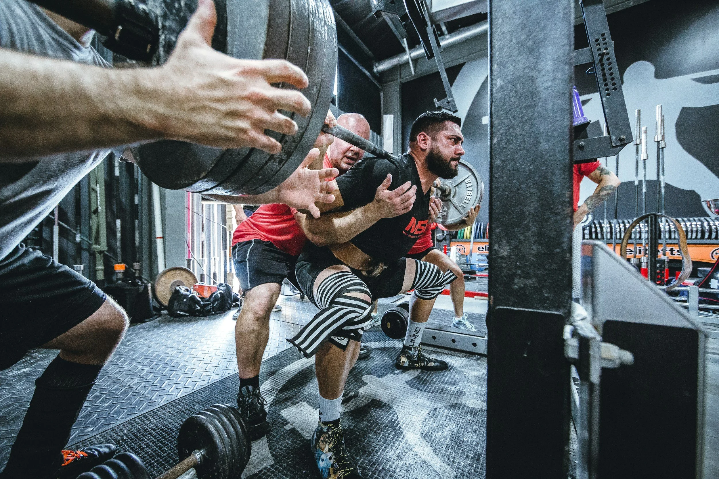 A lifter performing a barbell squat with spotters nearby