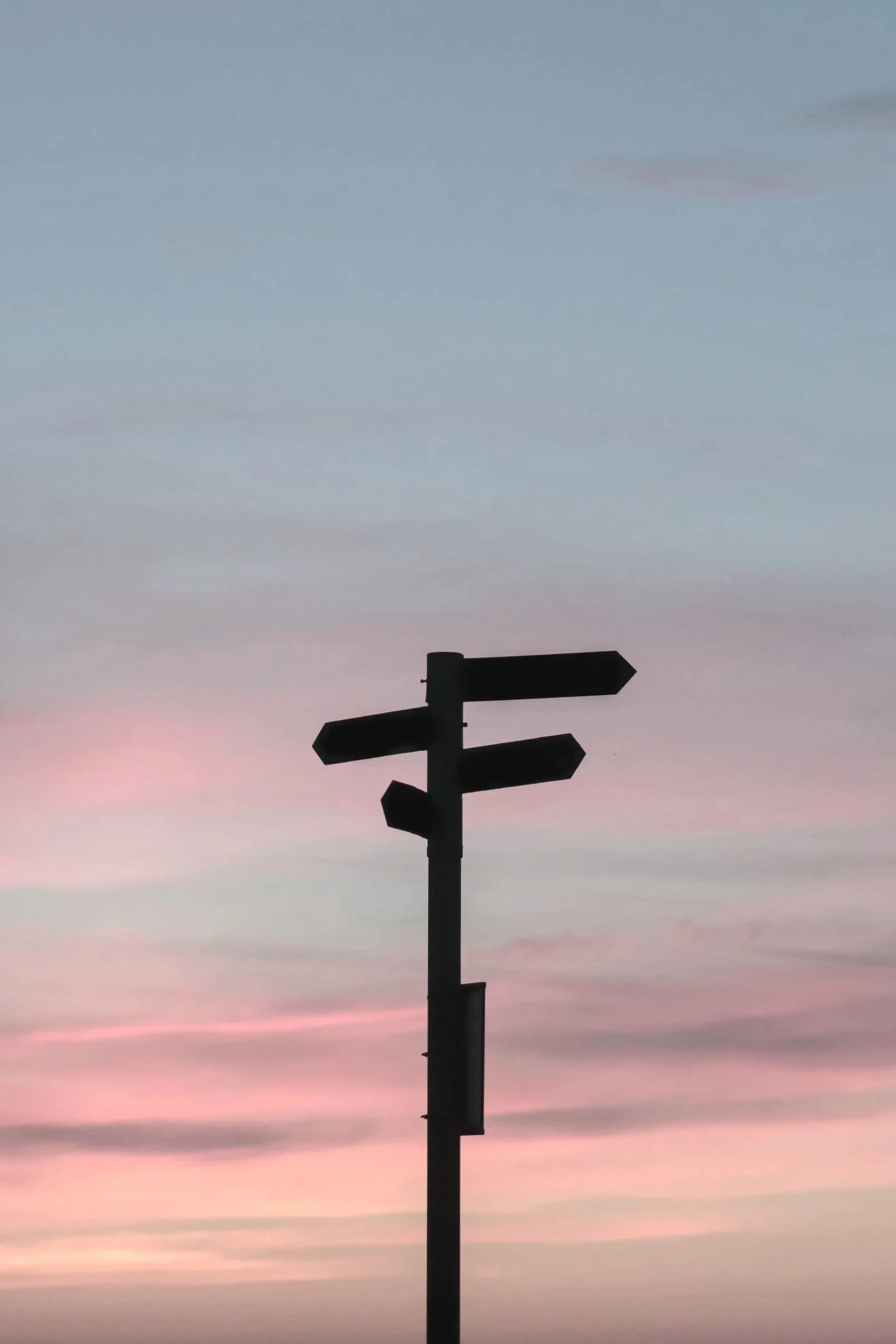 Silhouette of a multi-directional signpost against a pastel-colored sky during sunset.