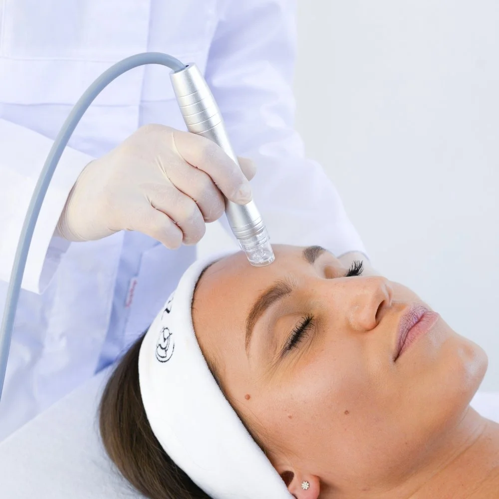 A woman receiving a facial treatment with a handheld device from a professional in a clinical setting.