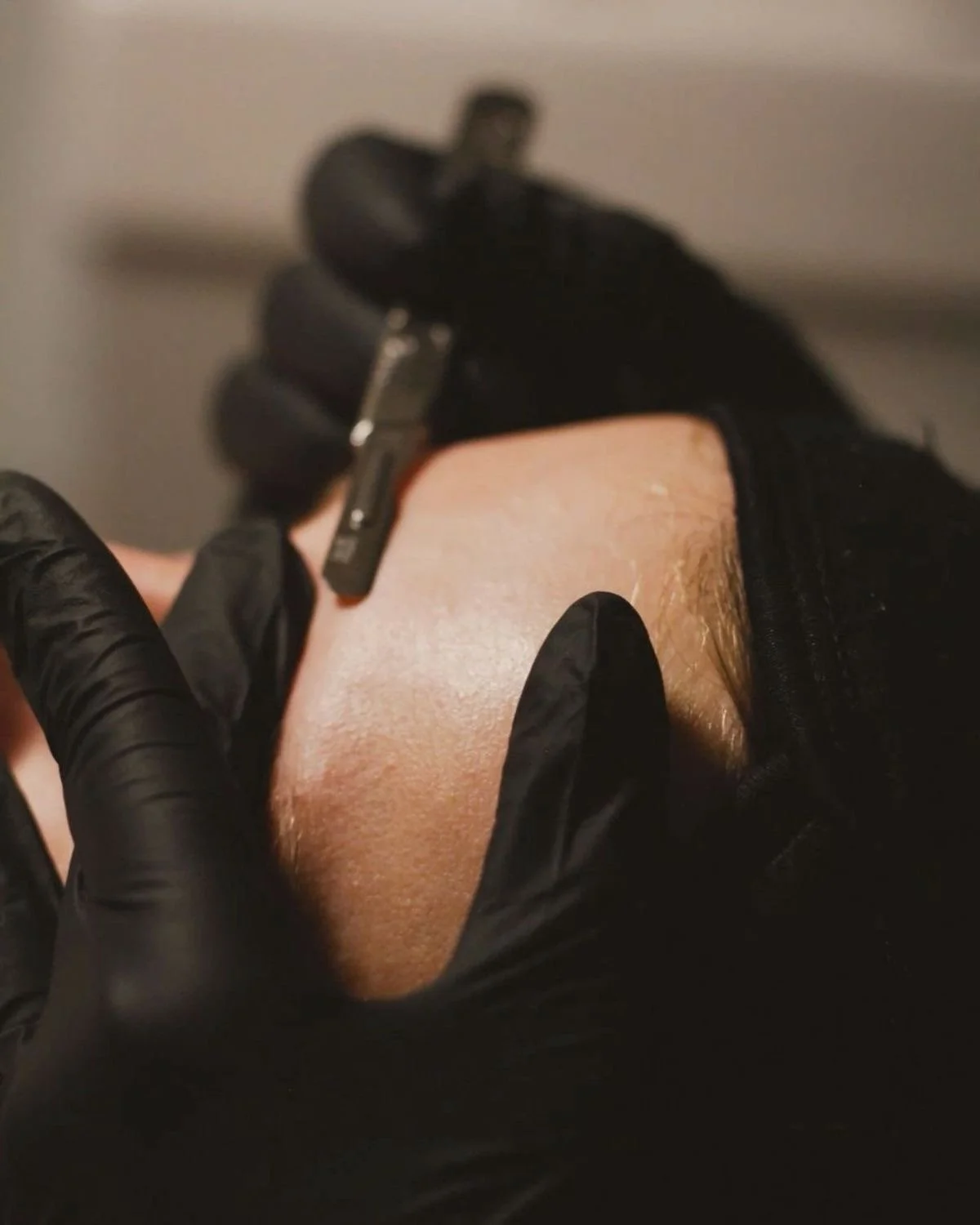 Tattoo artist wearing black gloves inking a tattoo on a person's skin.
