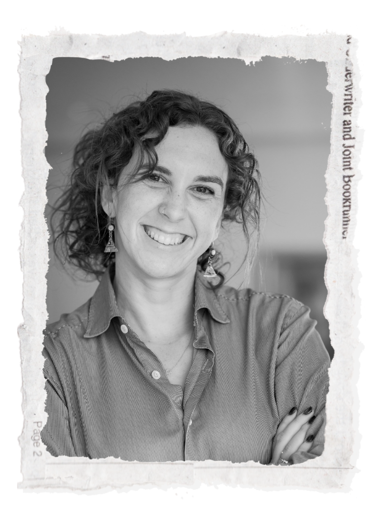 A woman with curly hair smiling, wearing a button-up shirt and earrings, in a black and white photo.