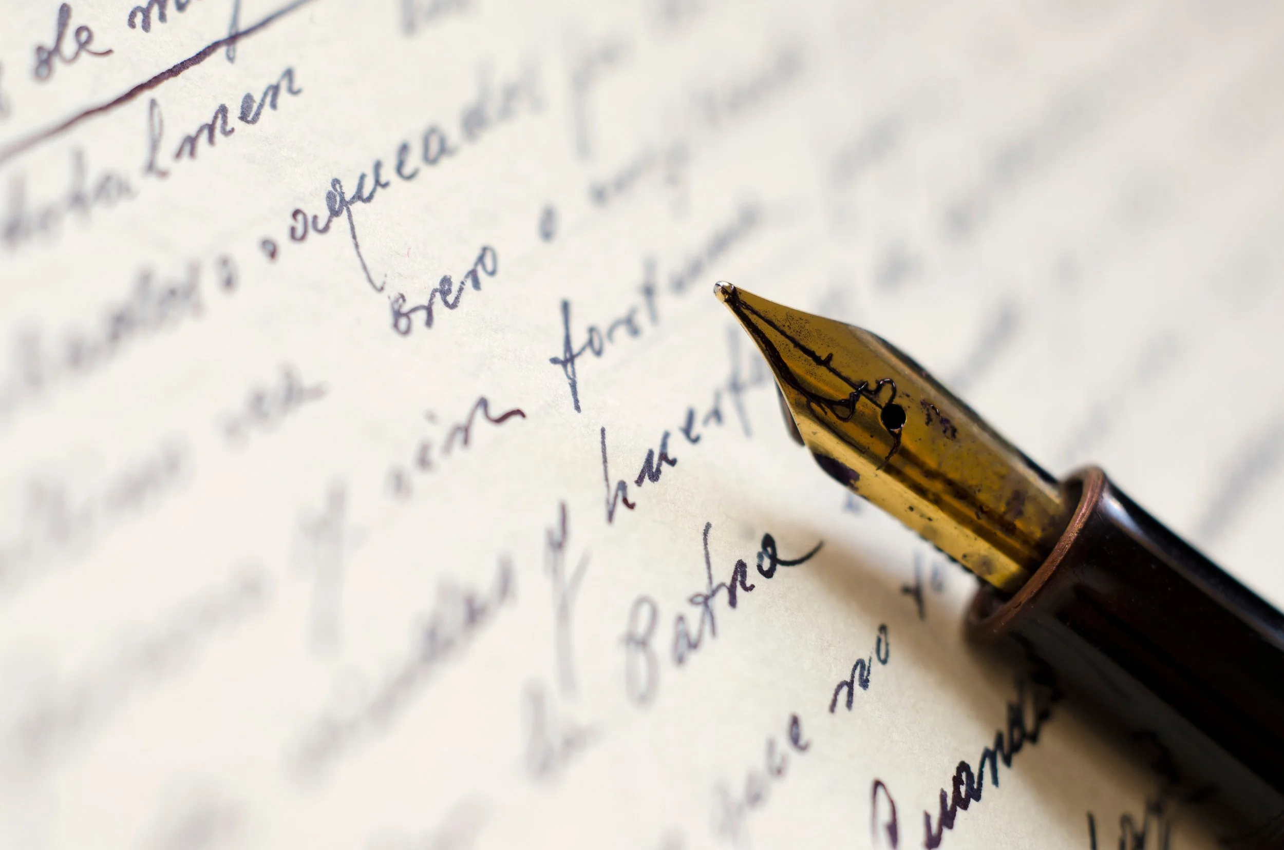 Close-up of a gold-tipped fountain pen resting on handwritten letter with cursive writing.