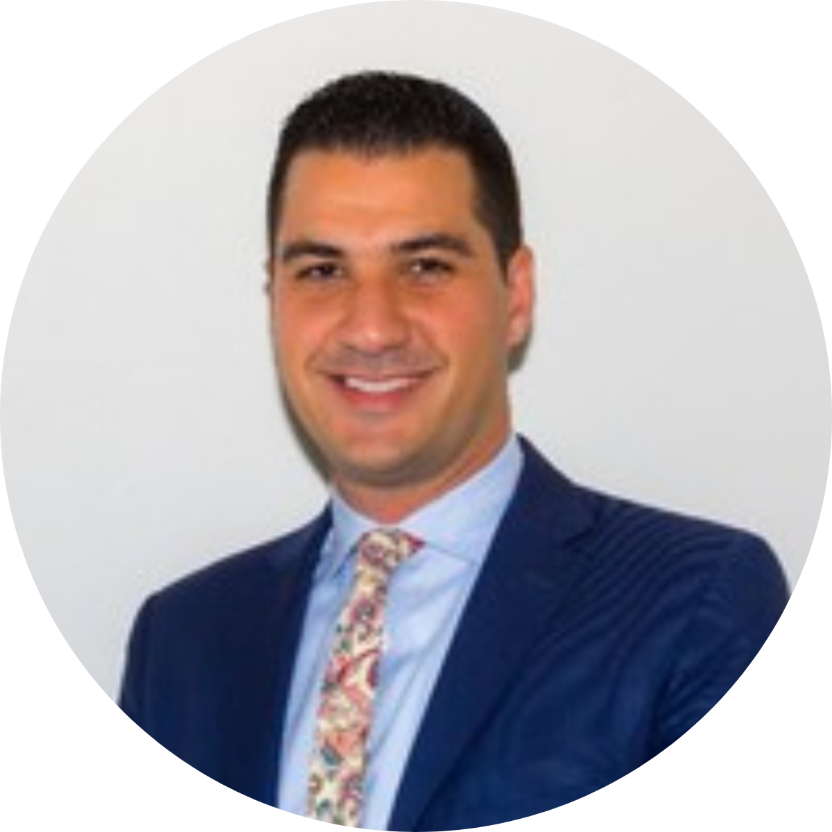 Professional portrait of a smiling man in a dark blue suit, light blue shirt, and a patterned tie.