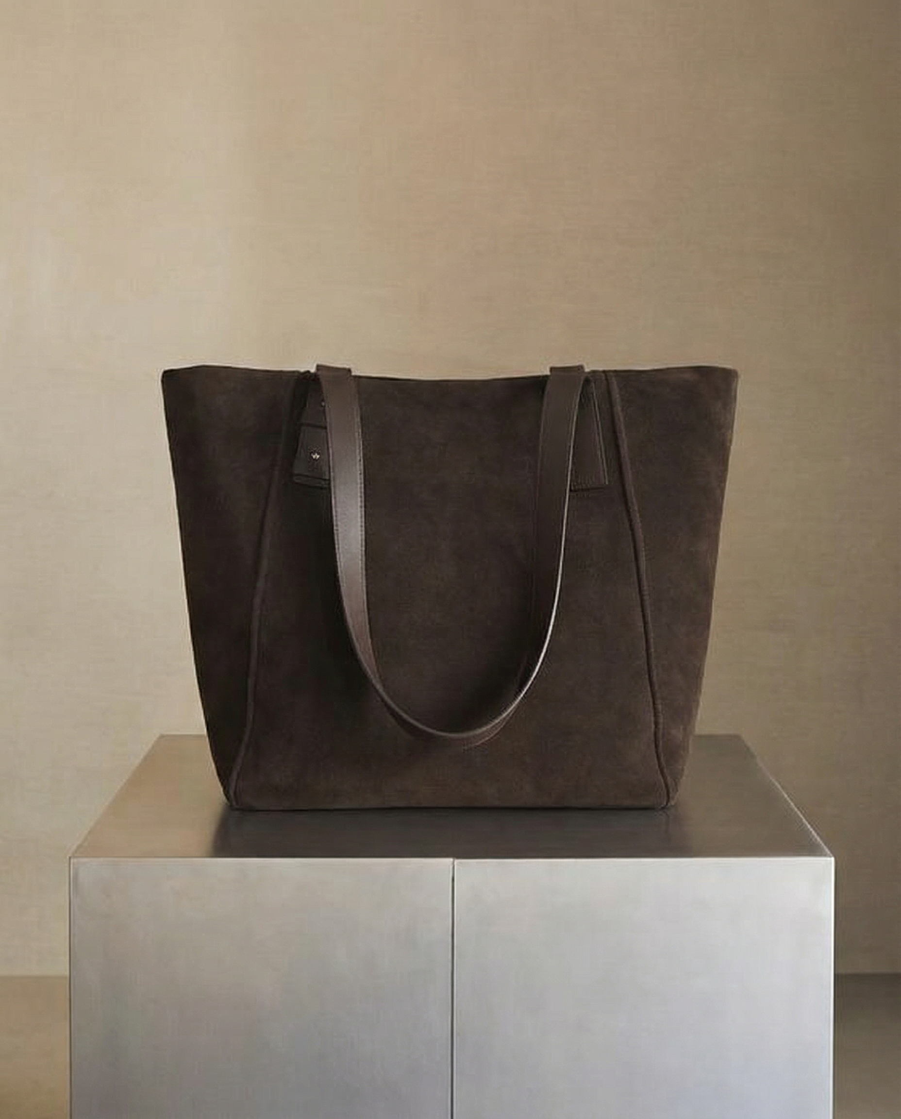 A black tote bag with long black handles displayed on a pedestal against a plain wall.  AI fashion editorial.