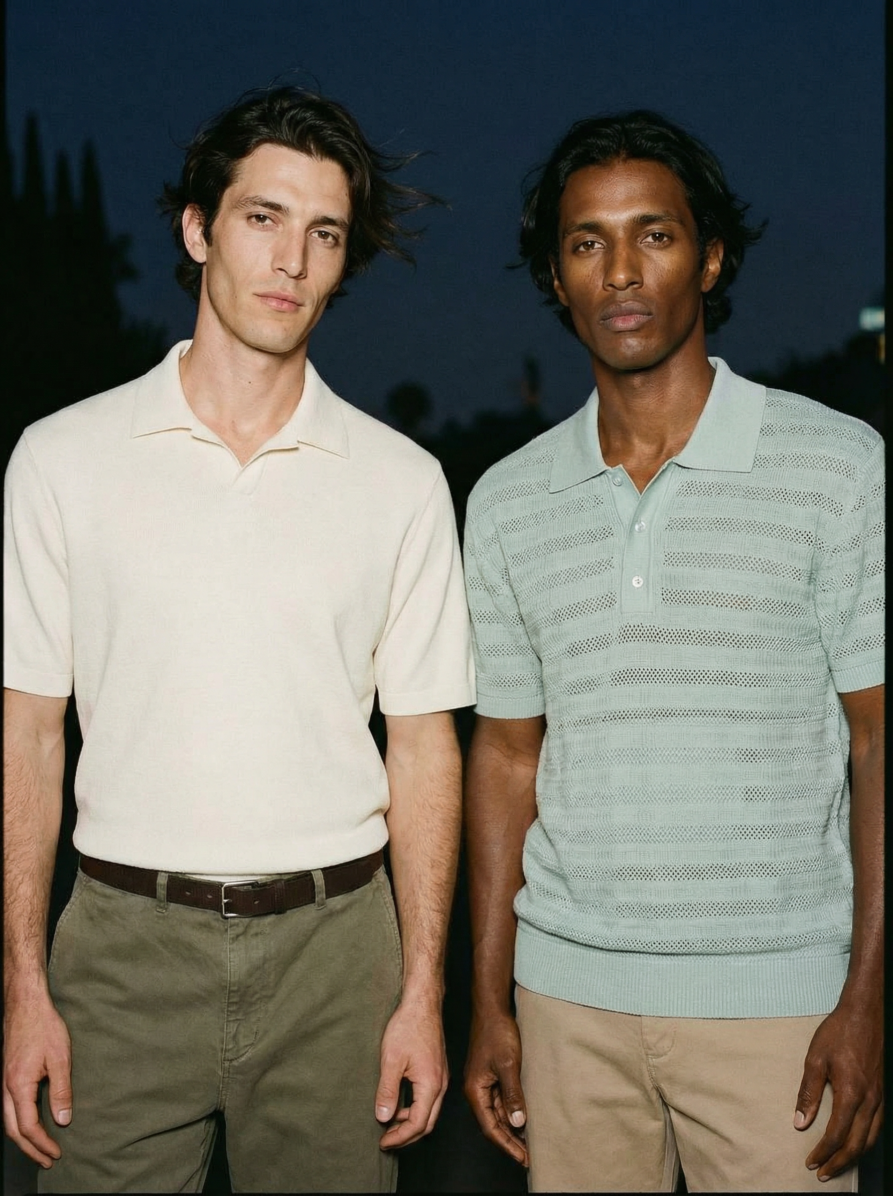 Two men standing side by side outdoors at night, holding hands.