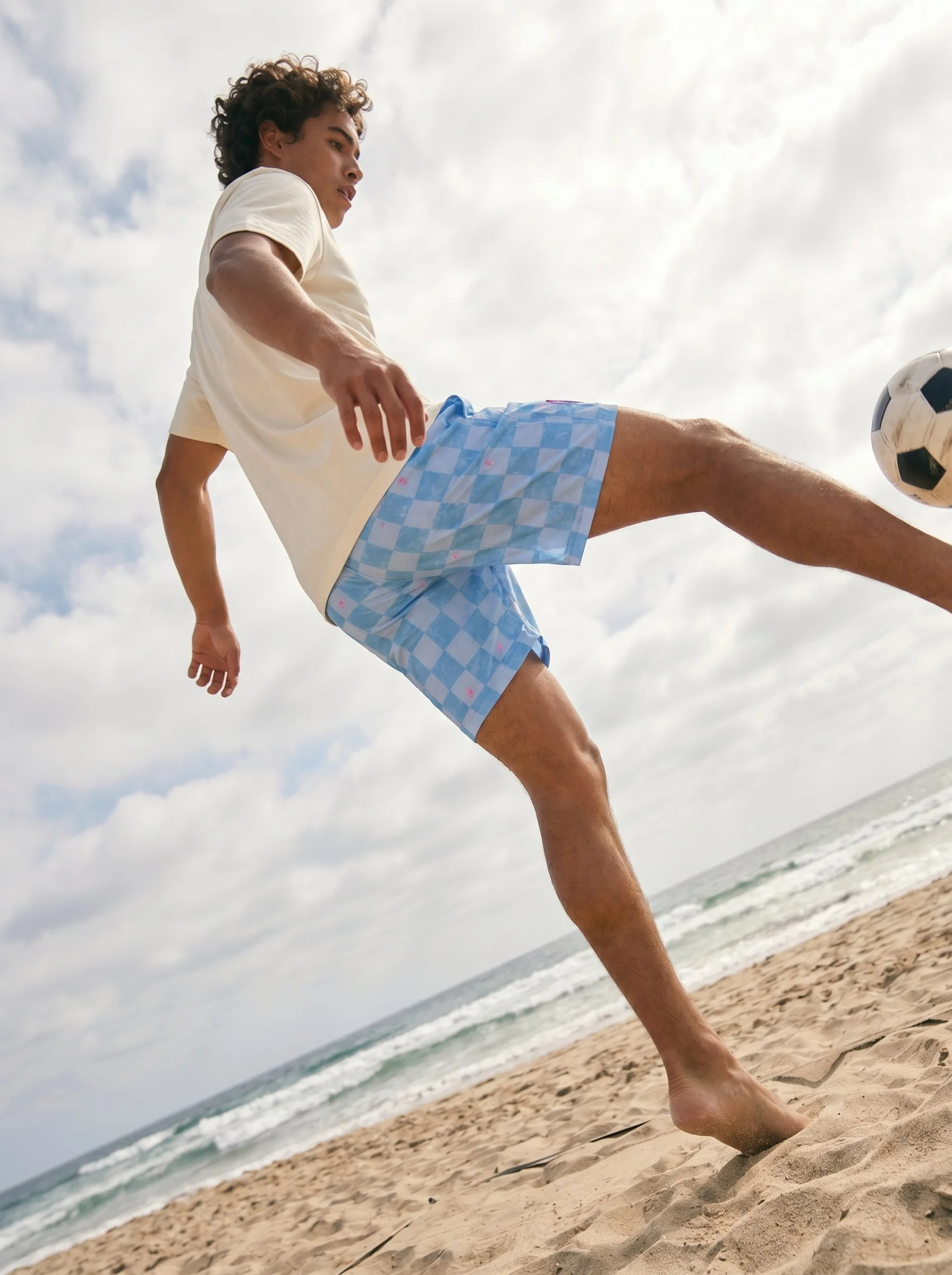 Young man playing soccer on the beach, kicking a soccer ball.
