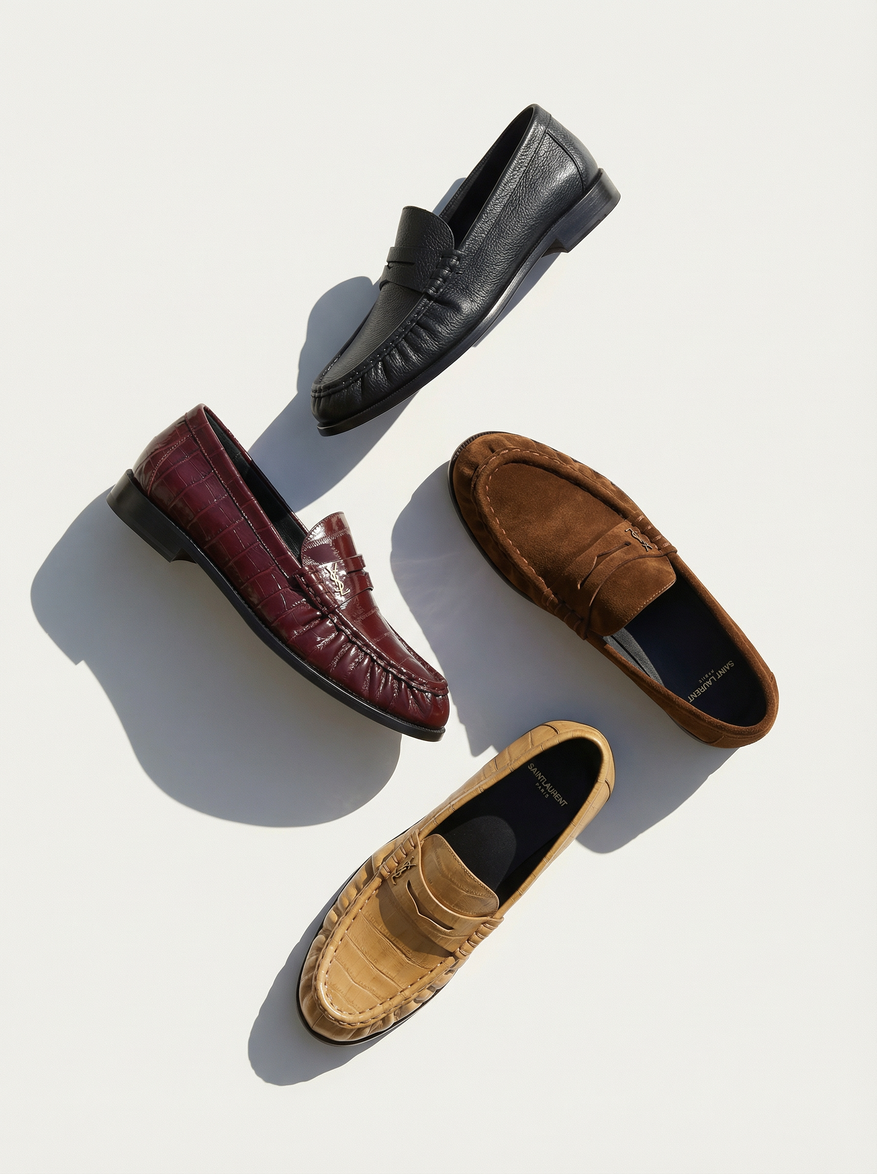 Five different men's loafers arranged on a white background. The shoes are in black, burgundy, brown, tan, and beige colors, with various textures including leather, suede, and crocodile pattern. AI fashion editorial.
