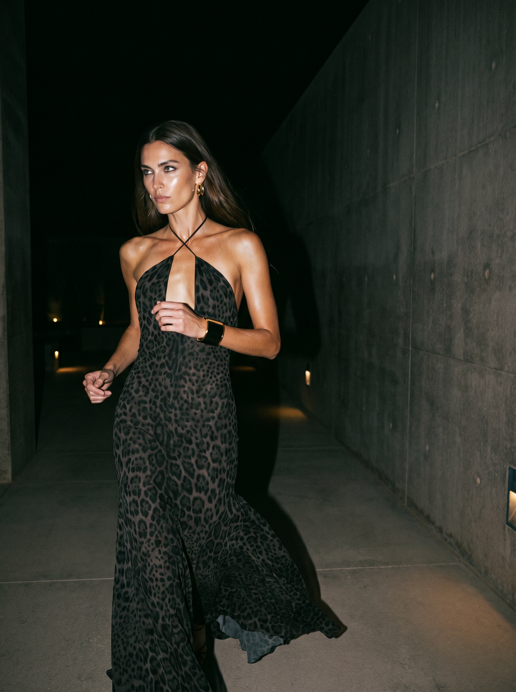 A woman in a leopard print dress walking outside at night.