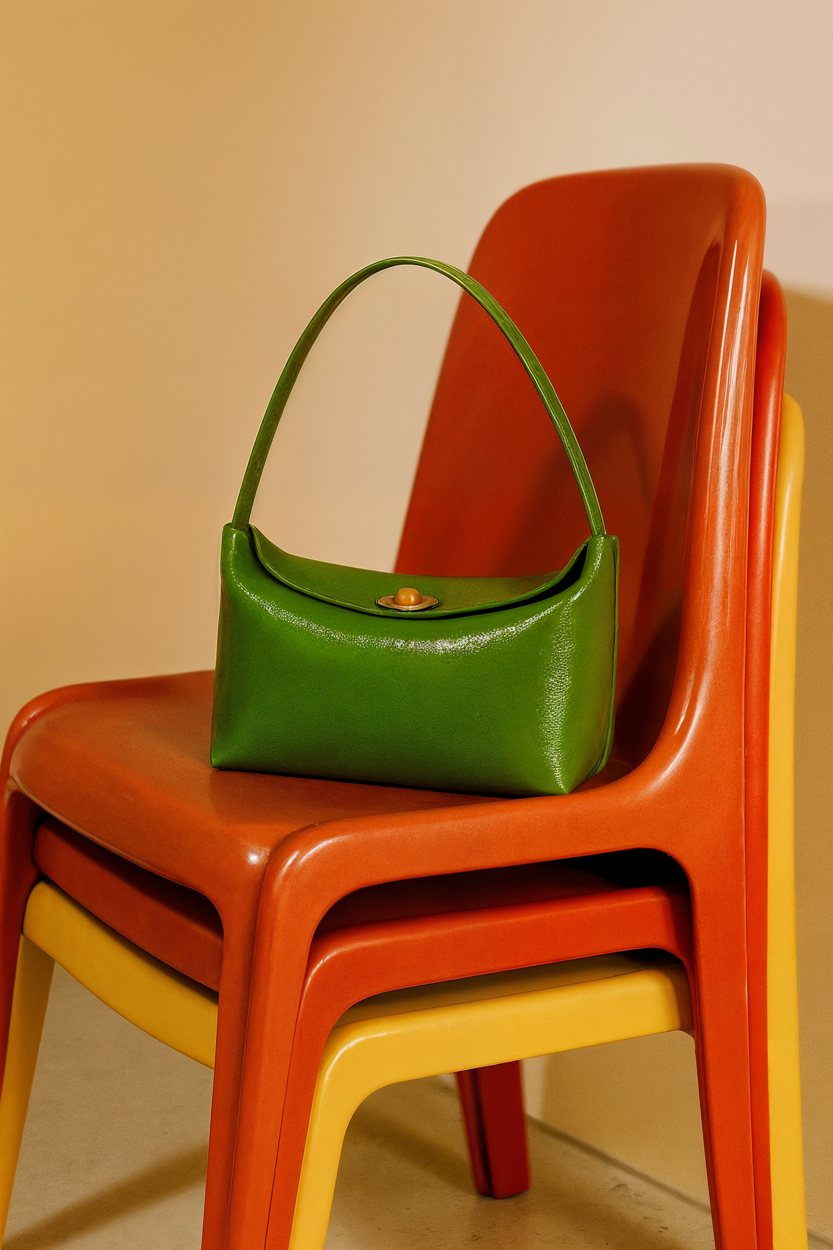 A stack of four colored chairs in yellow, orange, red, and green, with a green handbag resting on the top orange chair.