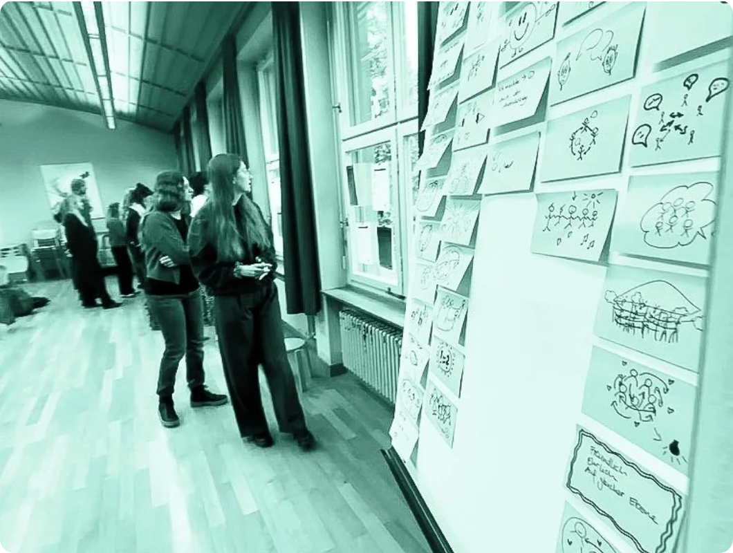 Schülerinnen und Schüler in einem Klassenraum, die sich Notizen und Zeichnungen an einer Wand mit Post-its anschauen.