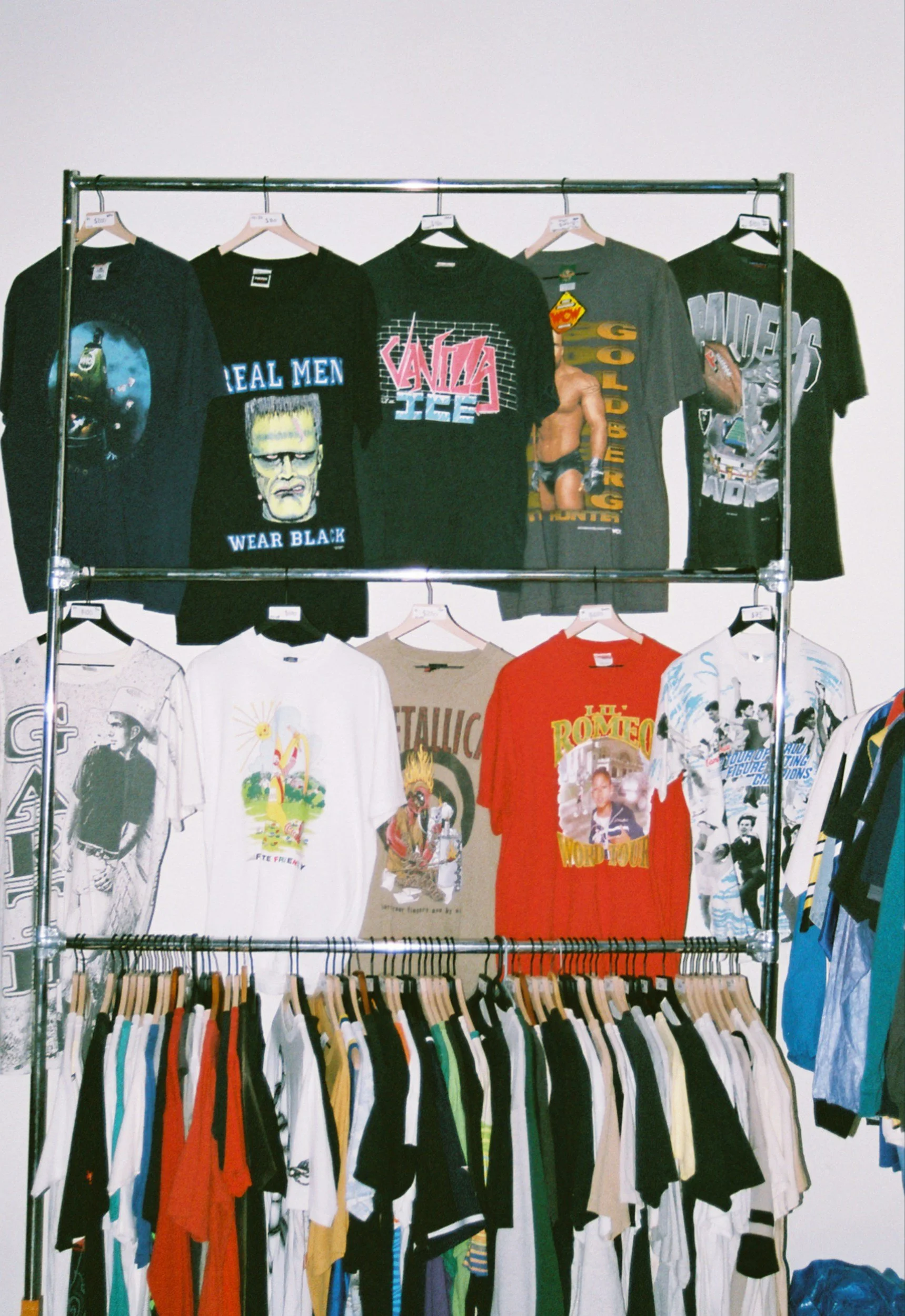 Clothing display featuring graphic T-shirts on hangers with cartoon characters, musicians, and pop culture references, arranged on a metal rack.