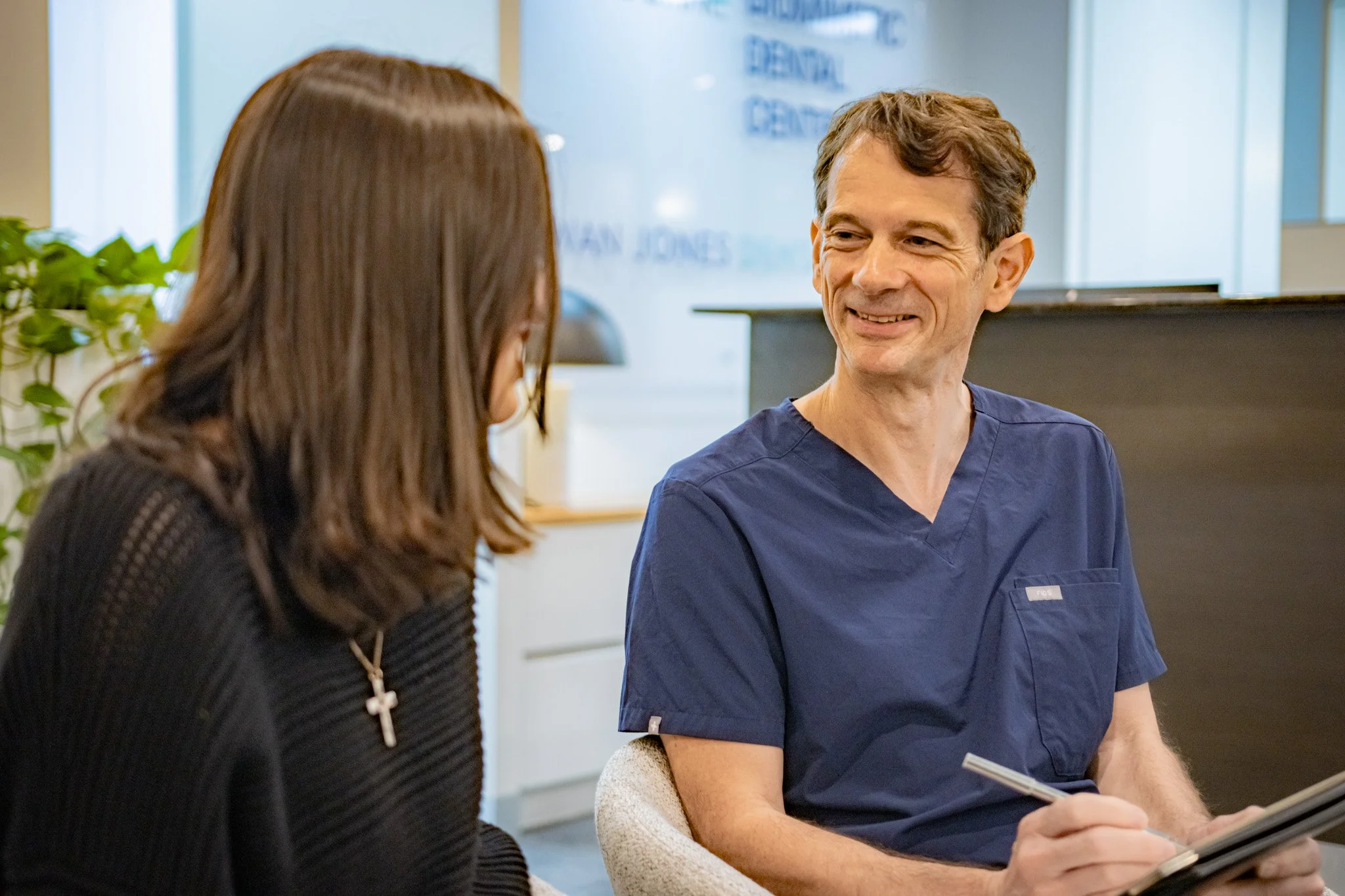 A doctor and a woman sitting in a clinic, engaged in conversation, with the doctor smiling.