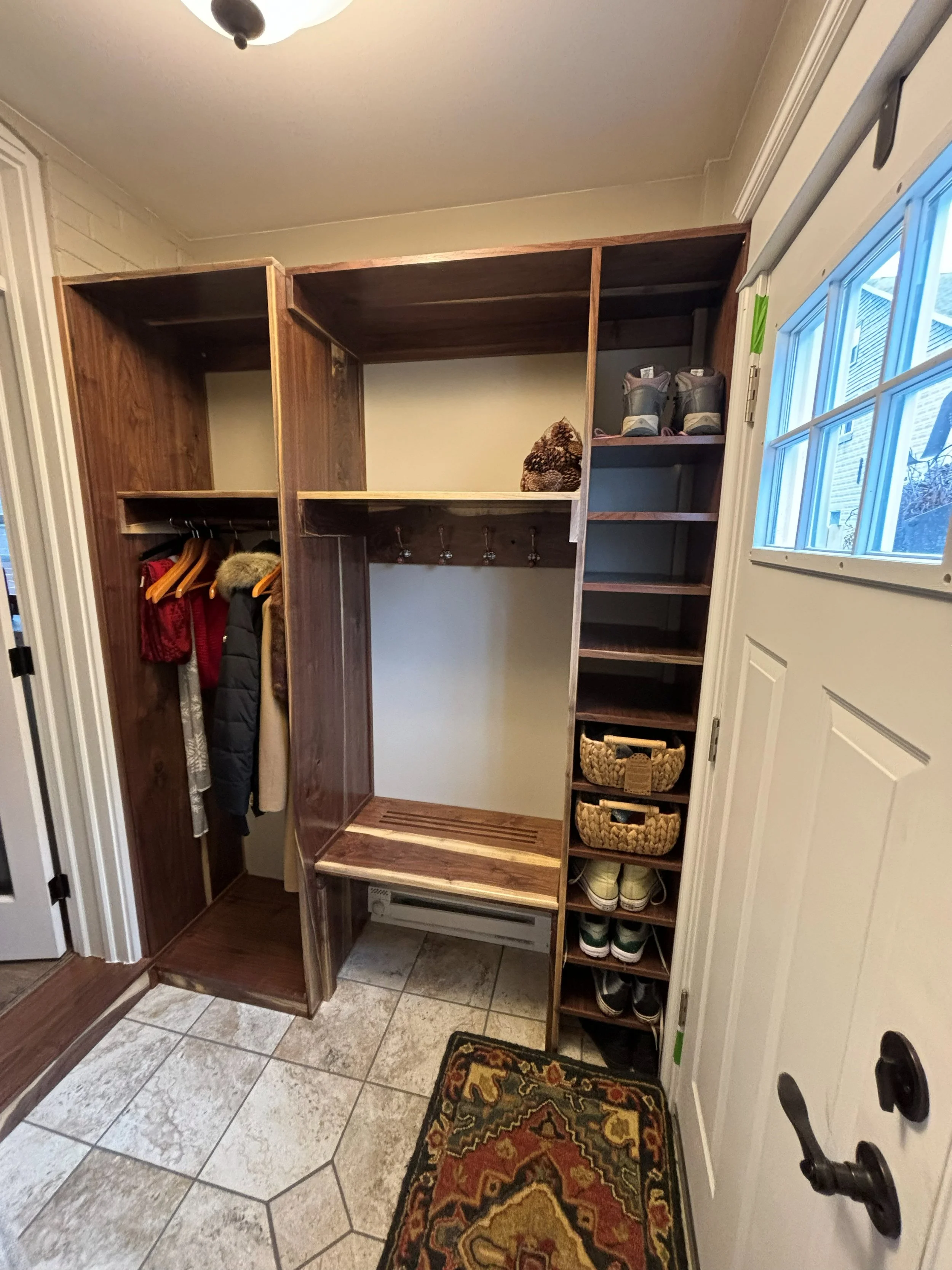 R.E. Arnold's Custom Construction. Walnut wooden storage closet with hooks, shelves, and cubbies for shoes.