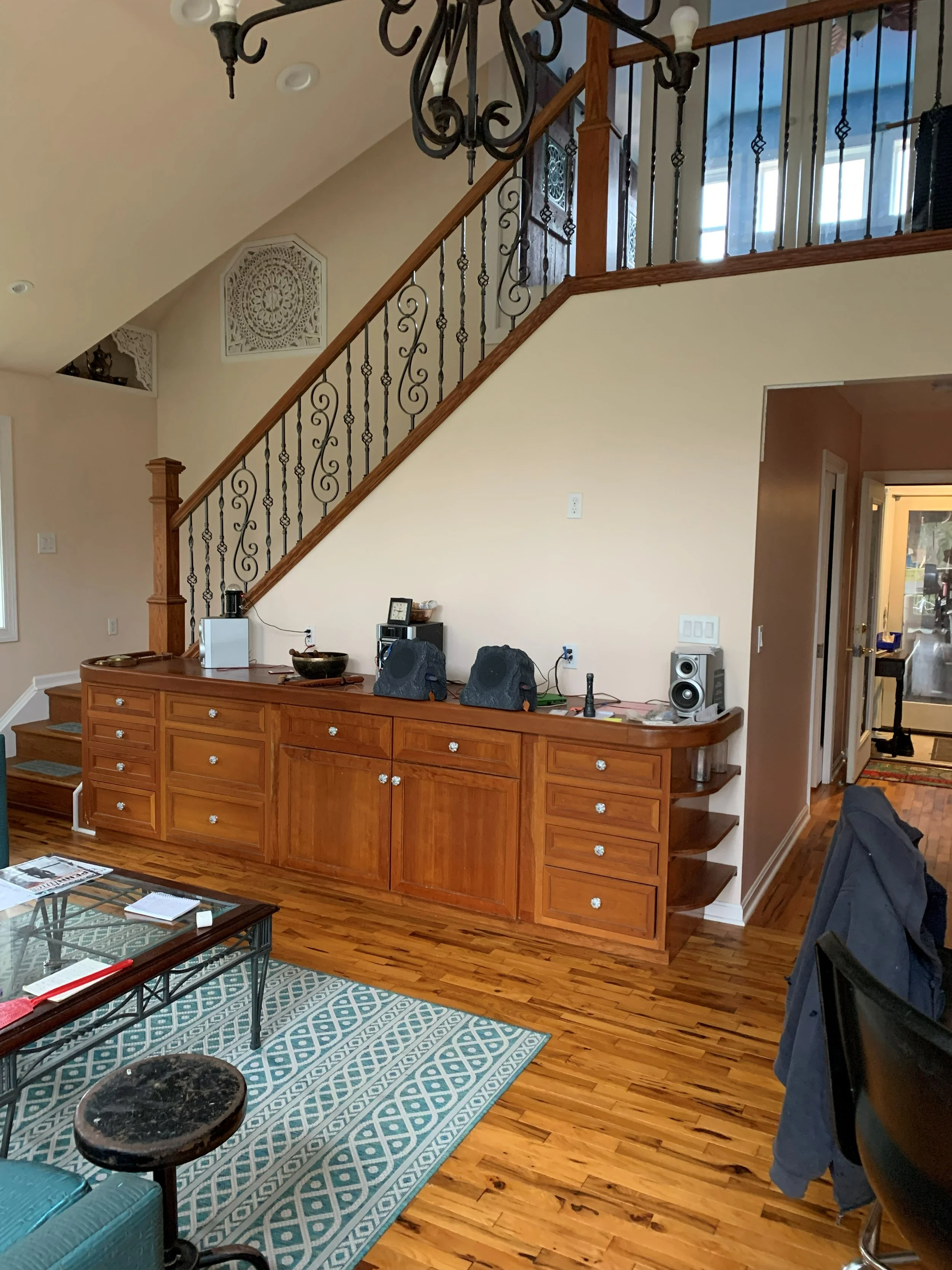 R.E. Arnold's Custom Construction. Living room with wooden floor and built-in wooden cabinet, staircase with decorative iron railing, and a chandelier hanging from the ceiling.